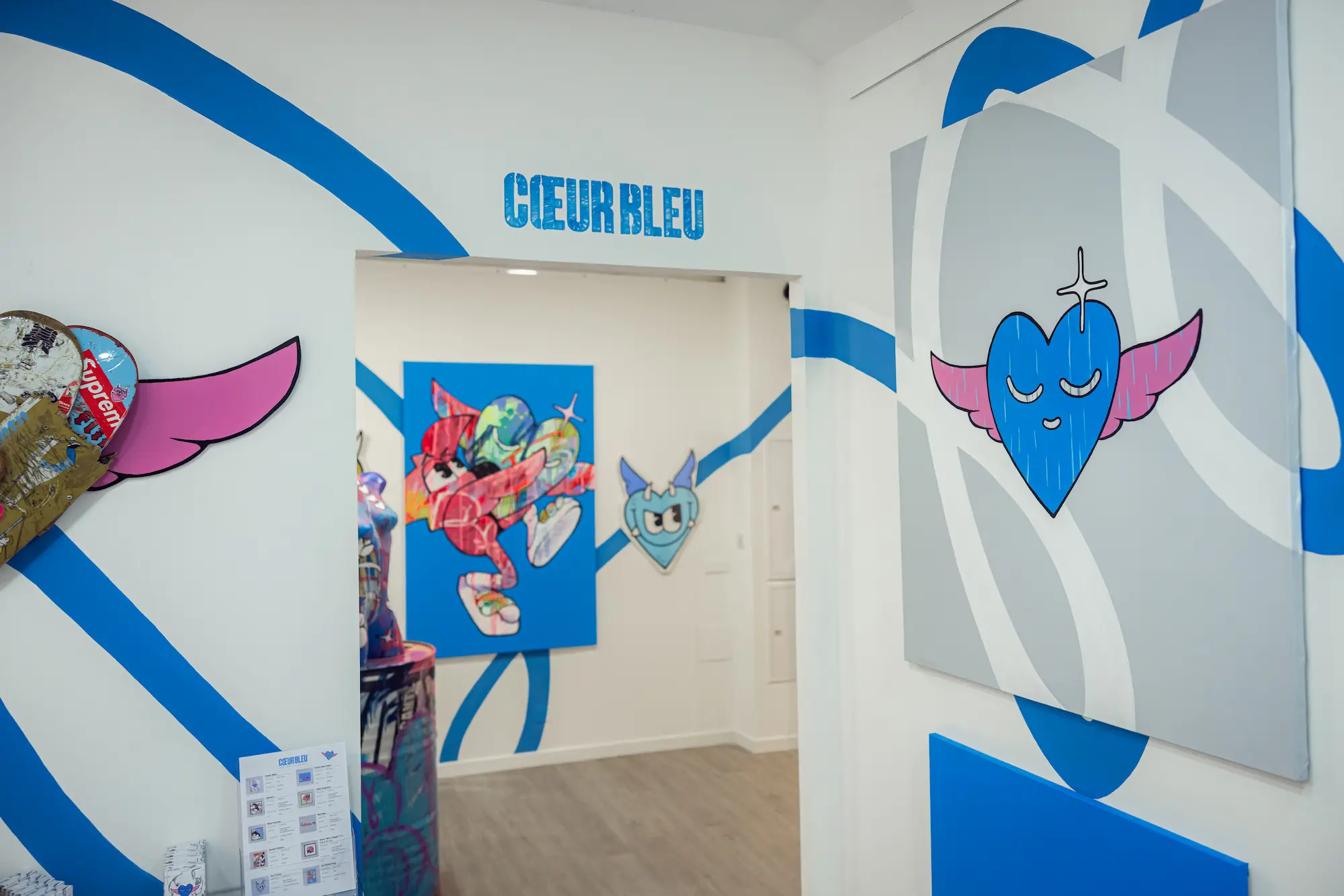 Entrée de l'exposition Cœur Bleu : titre peint au mur, lignes bleues et toile au cœur bleu ailé de Hugo W2CJ