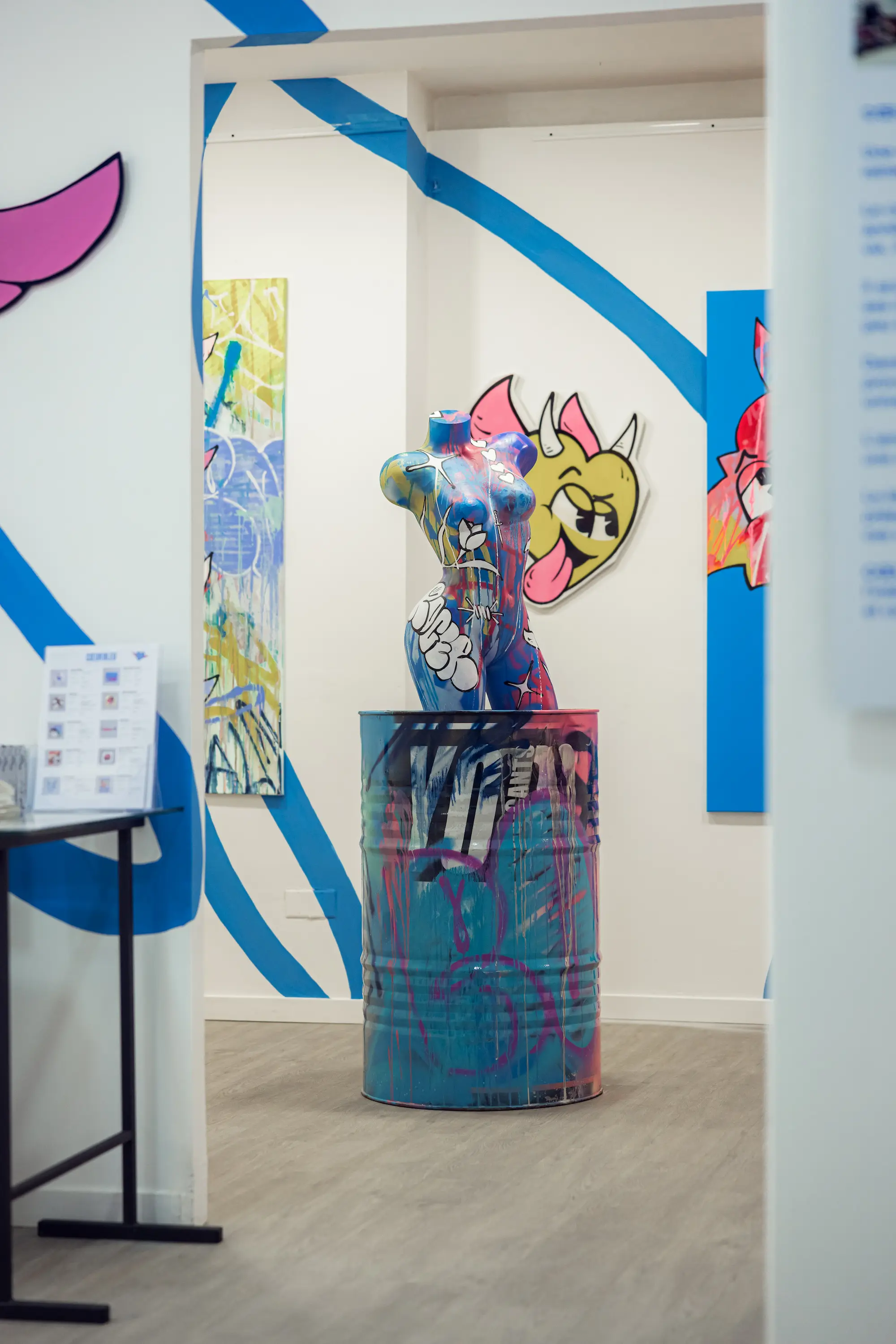 Buste féminin peint par Hugo W2CJ posé sur un bidon graffé, vu par l'embrasure d'une porte, exposition Cœur Bleu, Galerie Residenza, Bastia