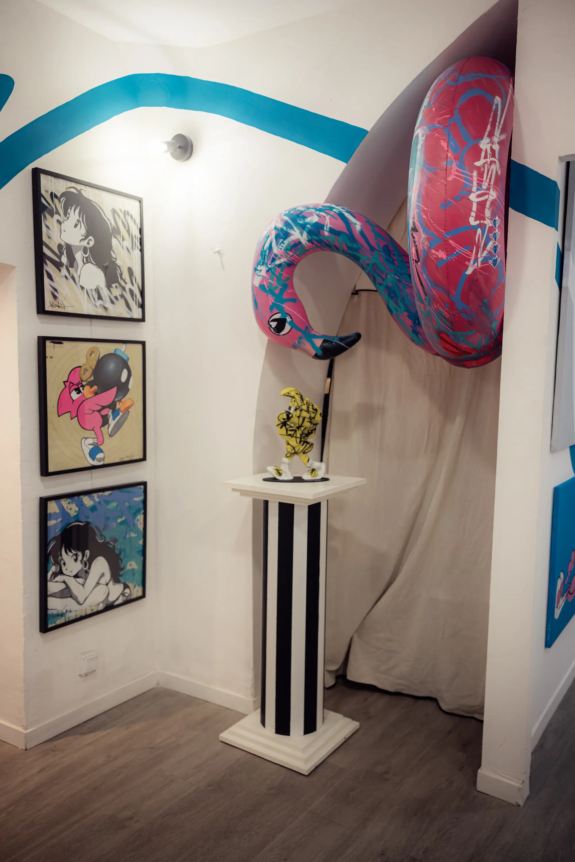 Angle de la galerie avec trois toiles encadrées et un flamant rose gonflable peint, suspendu au mur, exposition Cœur Bleu
