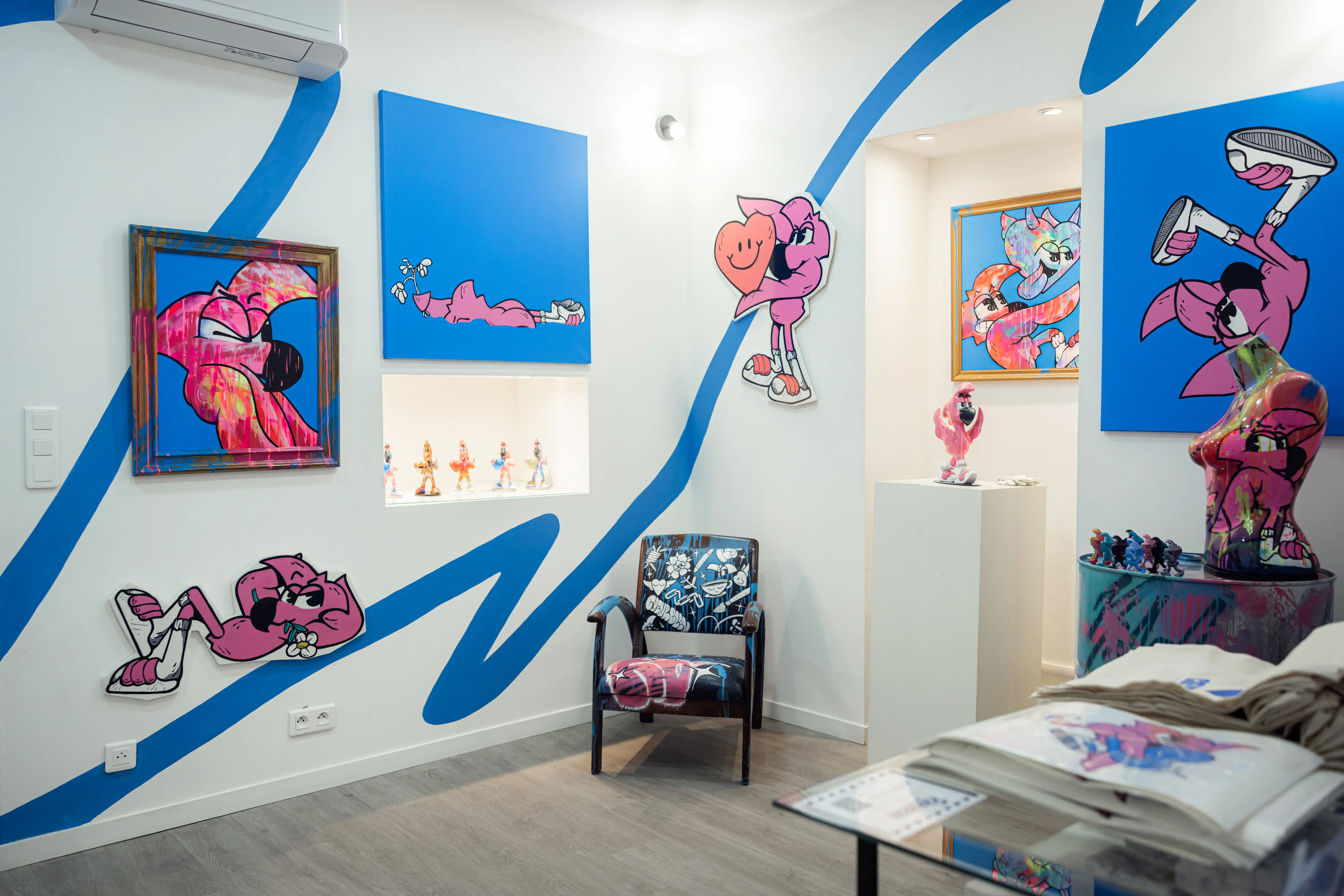Salle de l'exposition Cœur Bleu : toiles de Roger le Flamant Rose, découpes murales, chaise customisée et lignes bleues peintes au mur