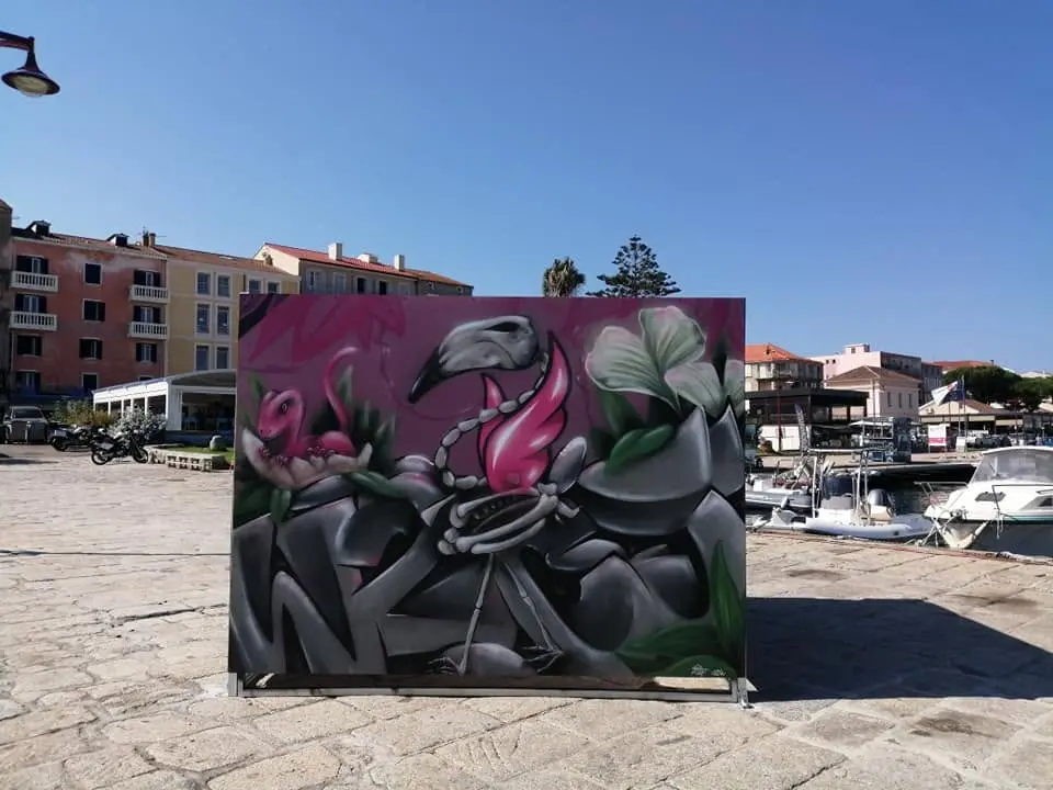 Live painting collectif au chapiteau Artpoval, 2019 : panneau graffiti posé sur le port, flamant squelette parmi des fleurs, bateaux en arrière-plan