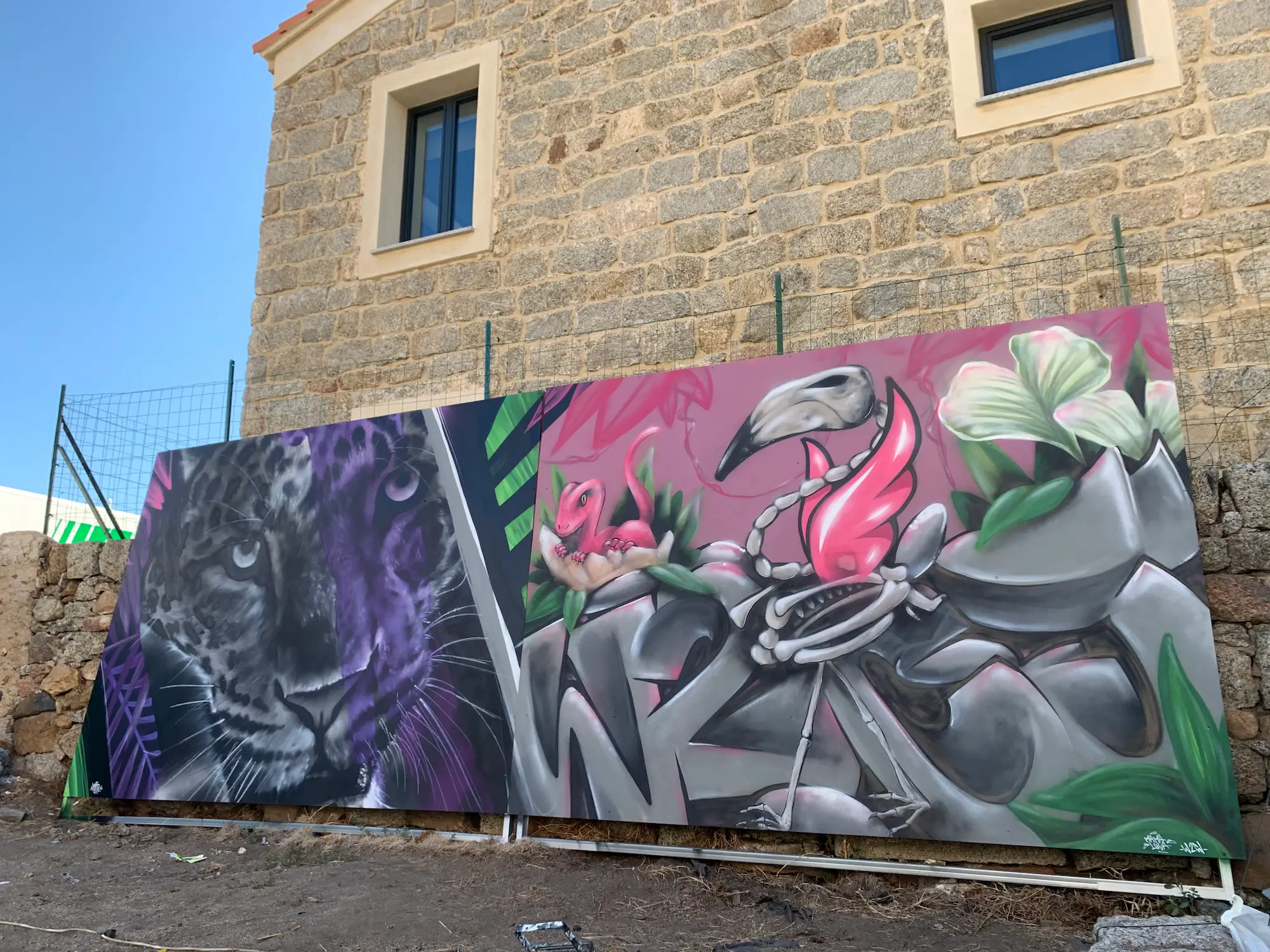 Live painting collectif au chapiteau Artpoval, 2019 : panneau graffiti, une panthère violette et un flamant squelette parmi des fleurs, devant un mur en pierre