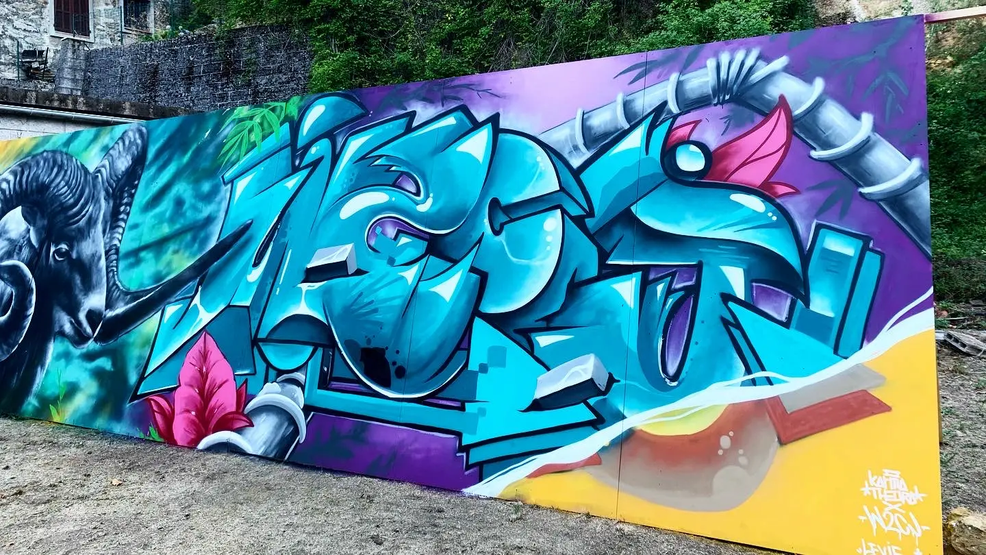 Live painting à Art'n Rocca, 2020 : fresque graffiti en lettrage turquoise et violet, un bélier peint à gauche, sur un long mur