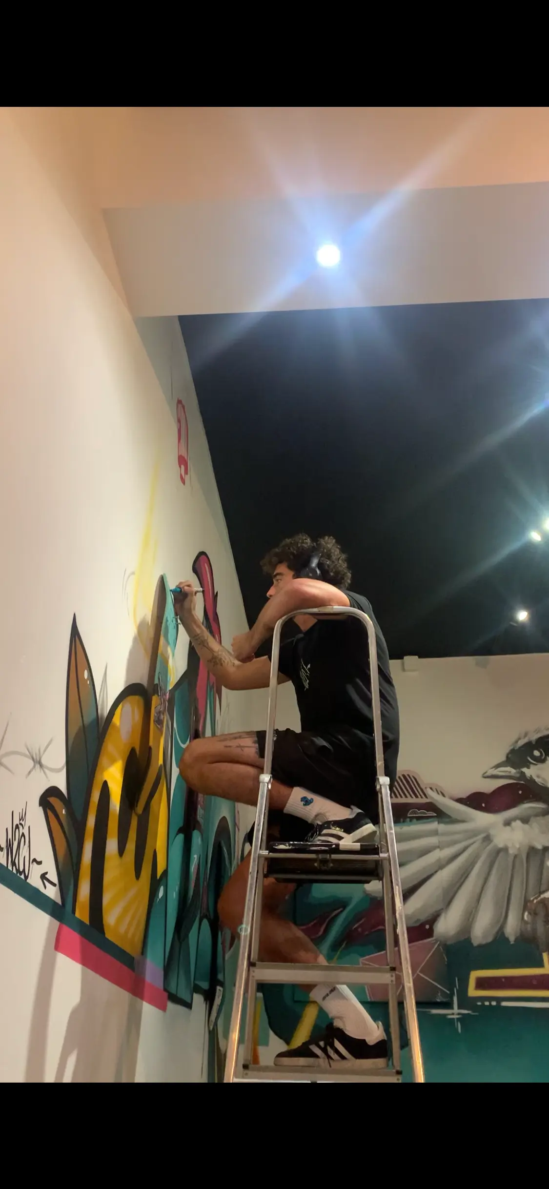 Exposition collective à La Conciergerie de Metz, 2020 : l'artiste sur un escabeau peignant la fresque murale de la salle