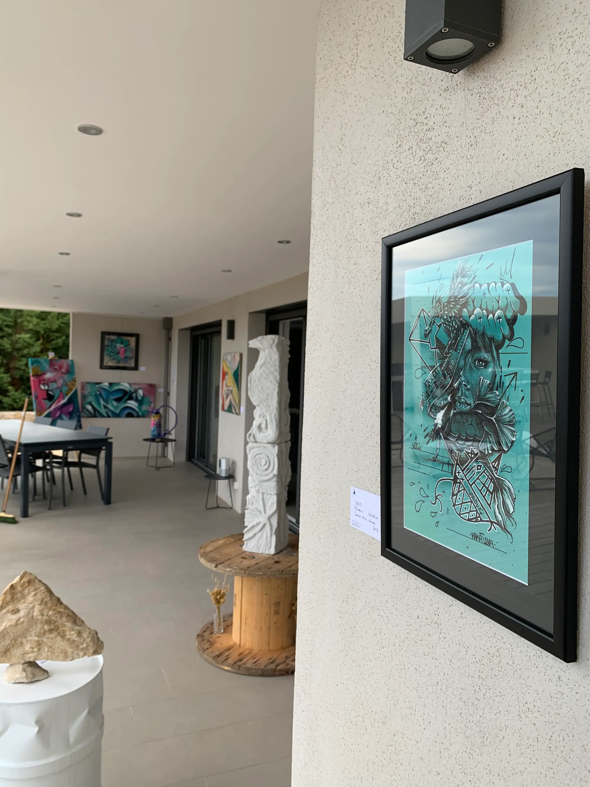 Résidence et exposition à la galerie Bel'arti, 2020 : œuvre encadrée sur fond turquoise accrochée sous la terrasse, sculpture totem blanche et toiles exposées au fond