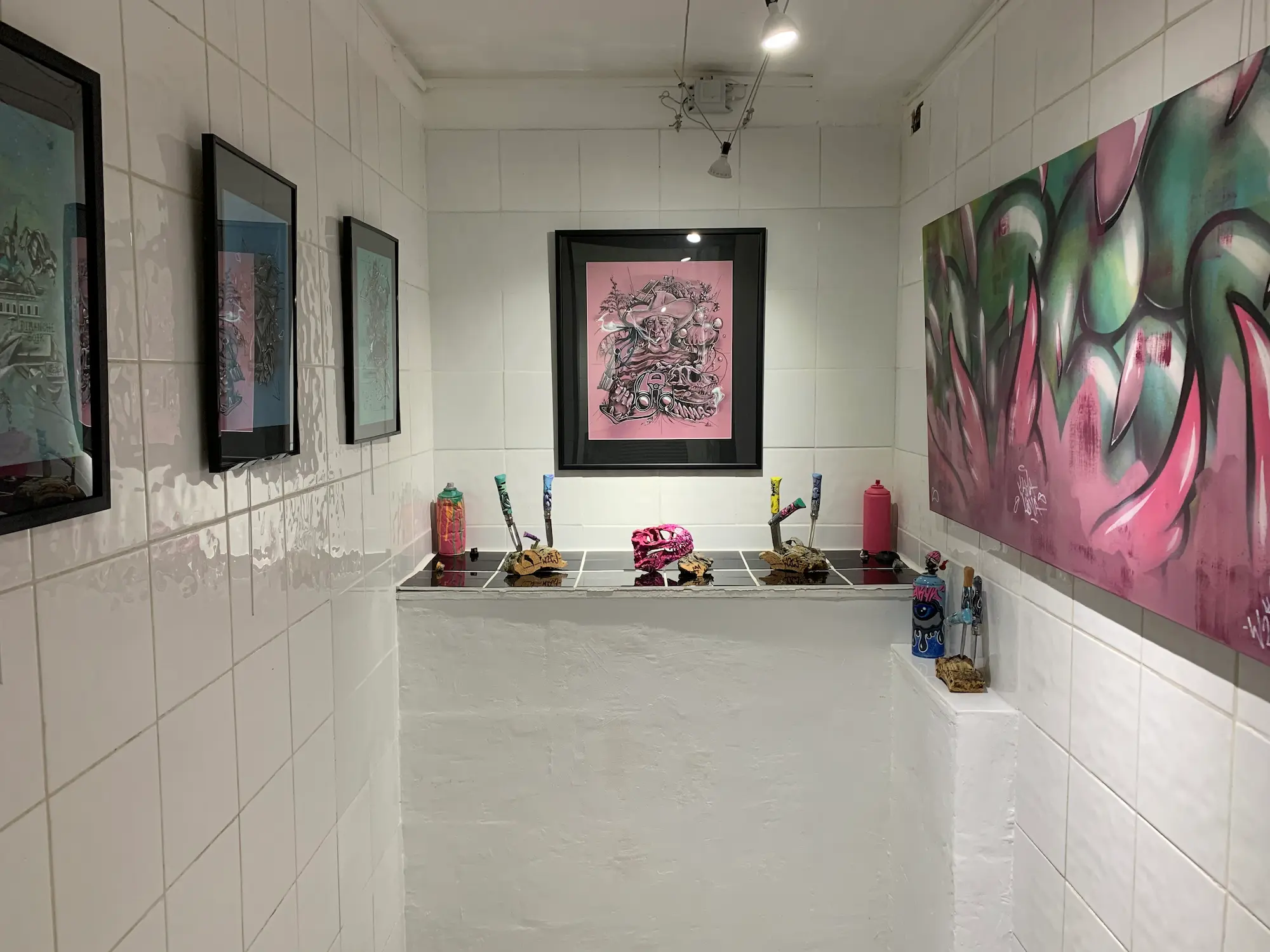 Exposition à la galerie Noir & Blanc, 2020 : salle d'exposition carrelée de blanc, œuvres encadrées roses, toile graffiti rose et vert et objets peints sur une étagère