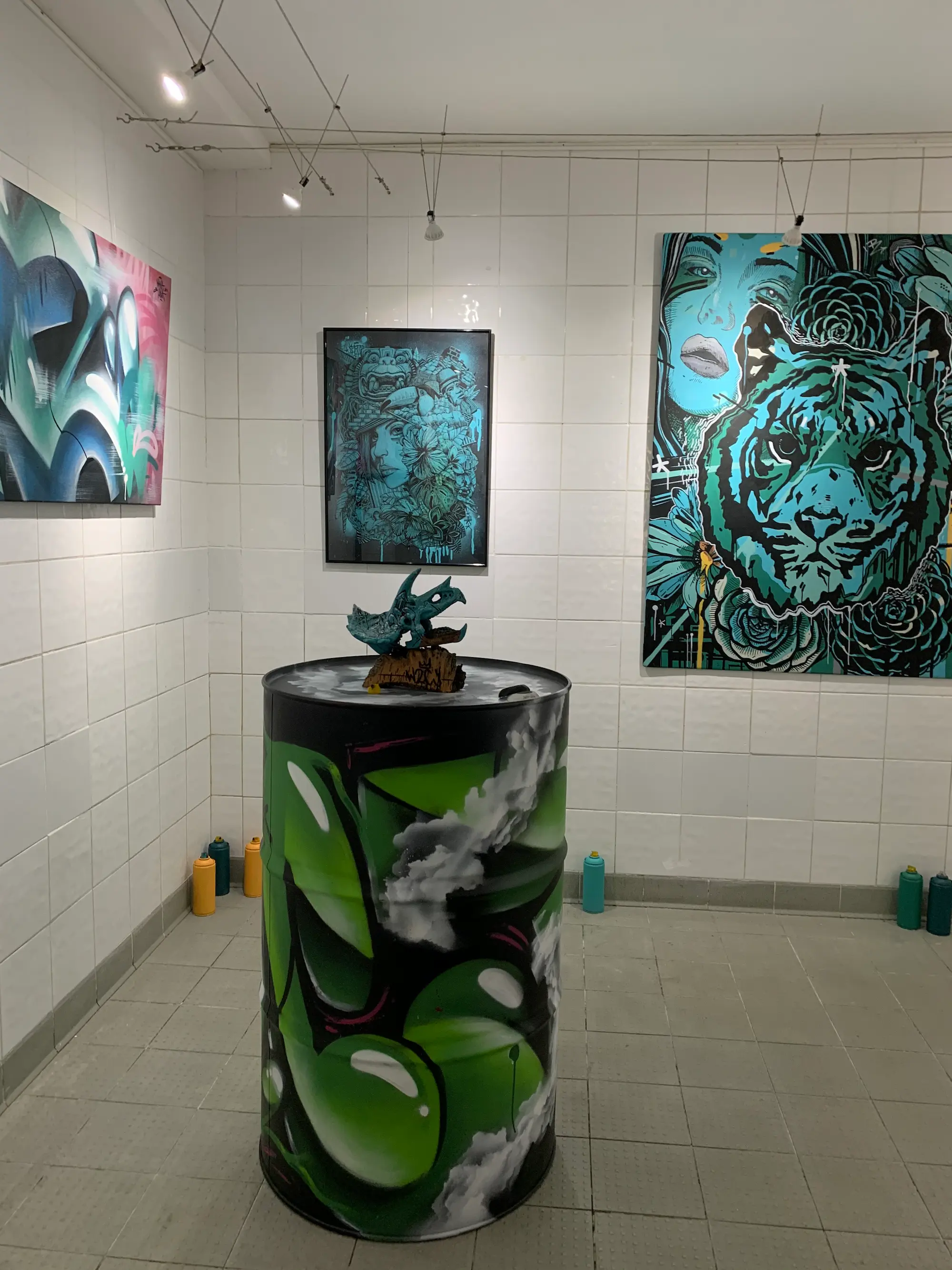 Exposition à la galerie Noir & Blanc, 2020 : salle d'exposition carrelée de blanc, bidon peint en vert, toile au tigre turquoise et toiles graffiti