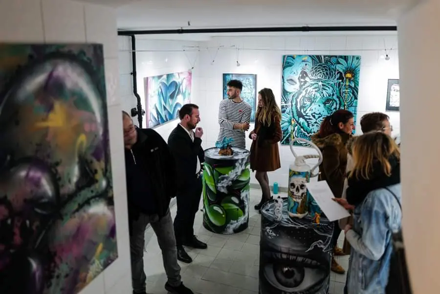 Exposition à la galerie Noir & Blanc, 2020 : visiteurs dans la salle d'exposition, toiles turquoise et bidons peints