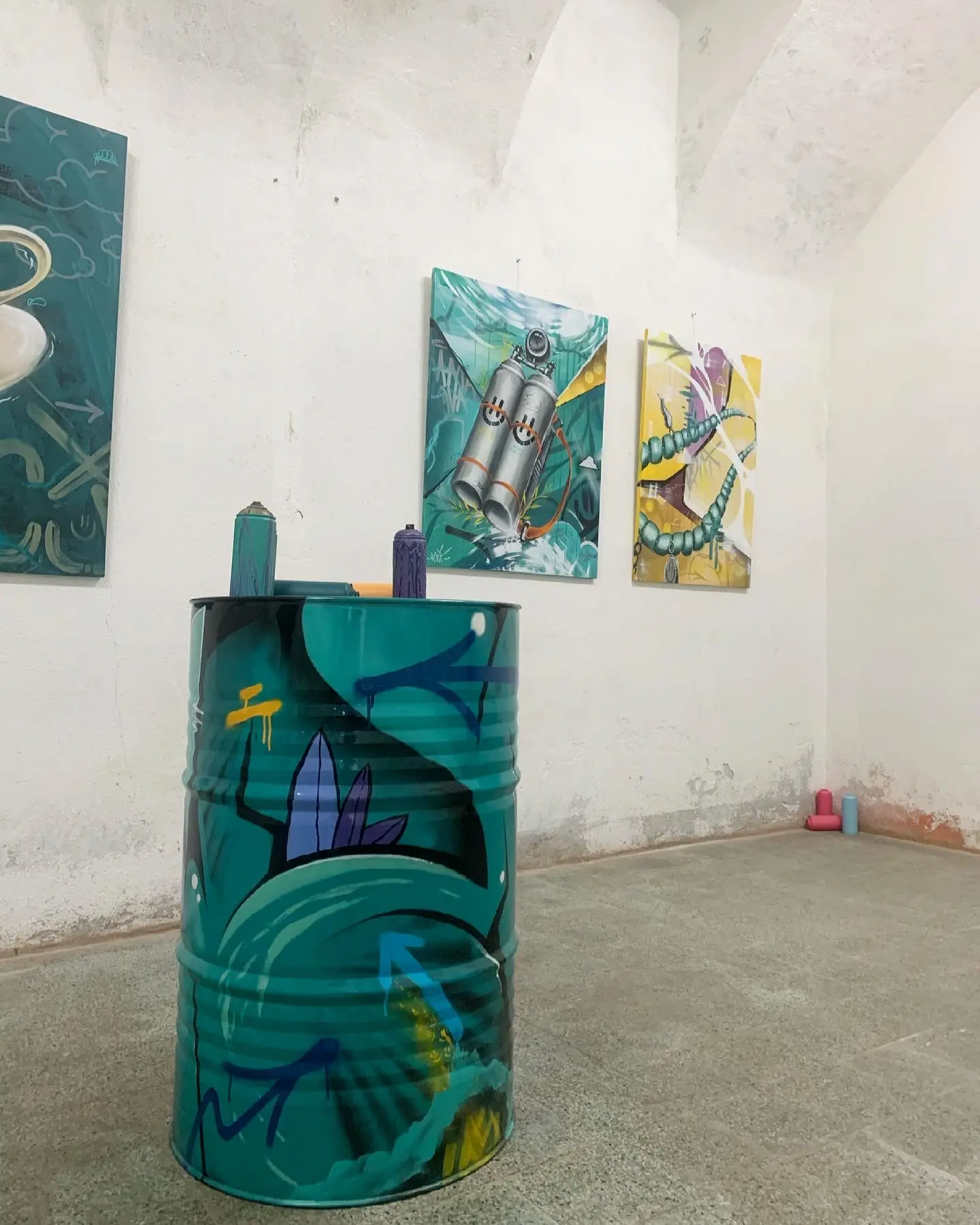 Exposition en duo avec Karma Theora, galerie Noir & Blanc, 2021 : bidon peint en turquoise devant des toiles accrochées sous une voûte blanche