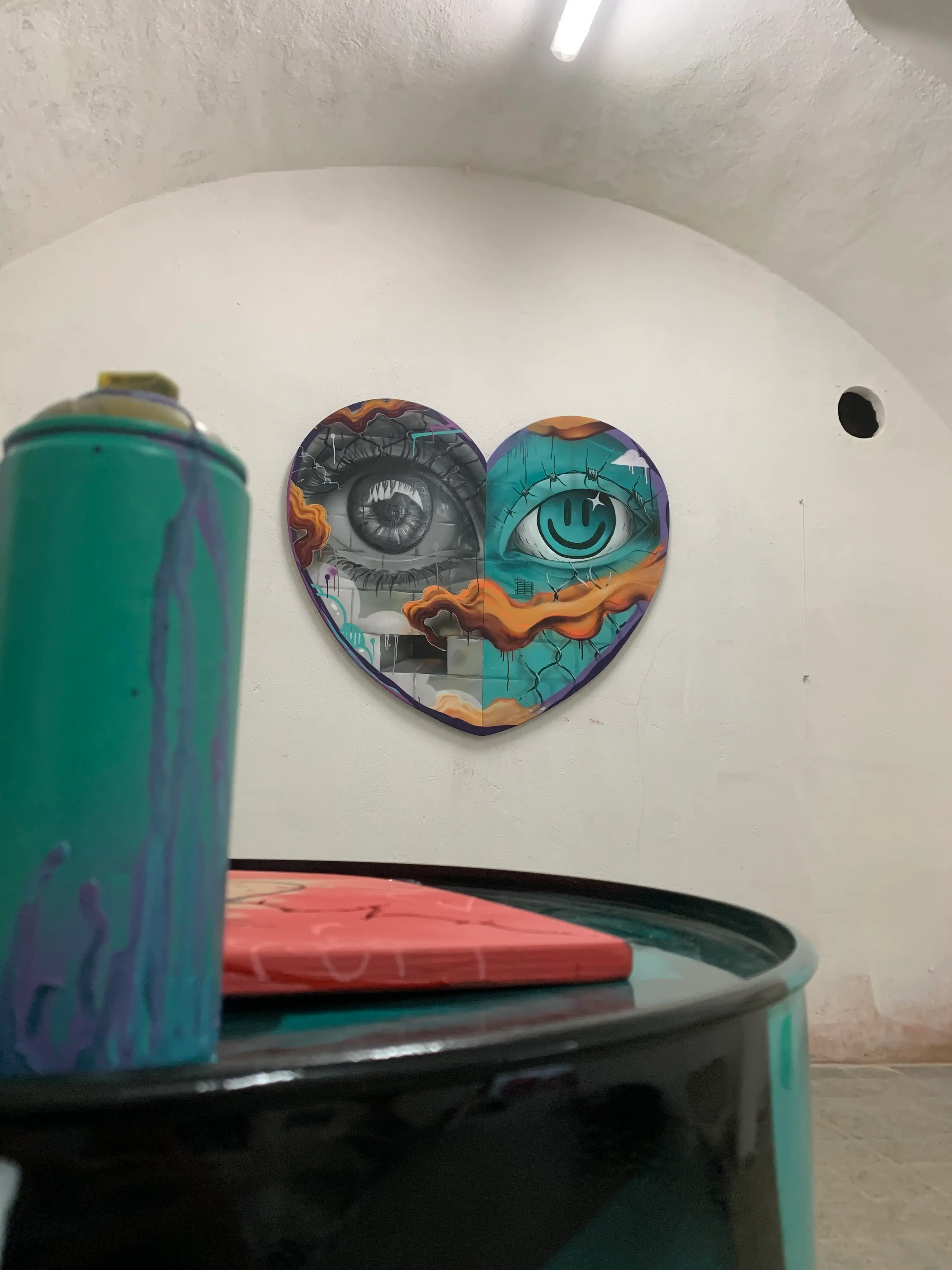 Exposition en duo avec Karma Theora, galerie Noir & Blanc, 2021 : toile en forme de cœur accrochée sous une voûte, une bombe de peinture turquoise au premier plan