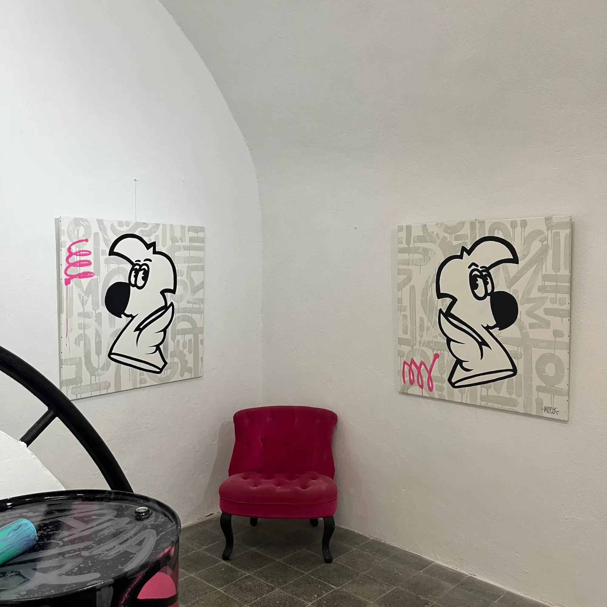 Exposition à la galerie Noir & Blanc, 2022 : deux toiles de Roger le Flamant Rose en noir et blanc sur fond de lettrage gris, de part et d'autre d'un fauteuil rose