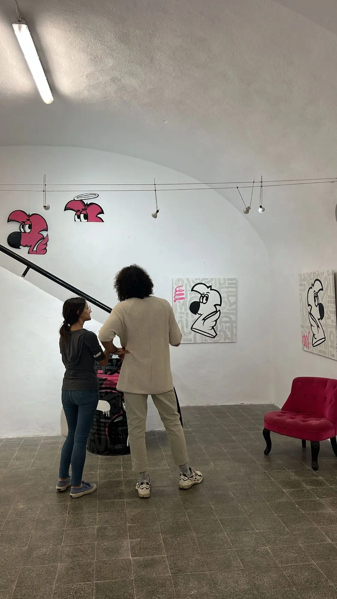 Exposition à la galerie Noir & Blanc, 2022 : deux visiteurs regardant l'accrochage, toiles de Roger le Flamant Rose et découpes roses au mur