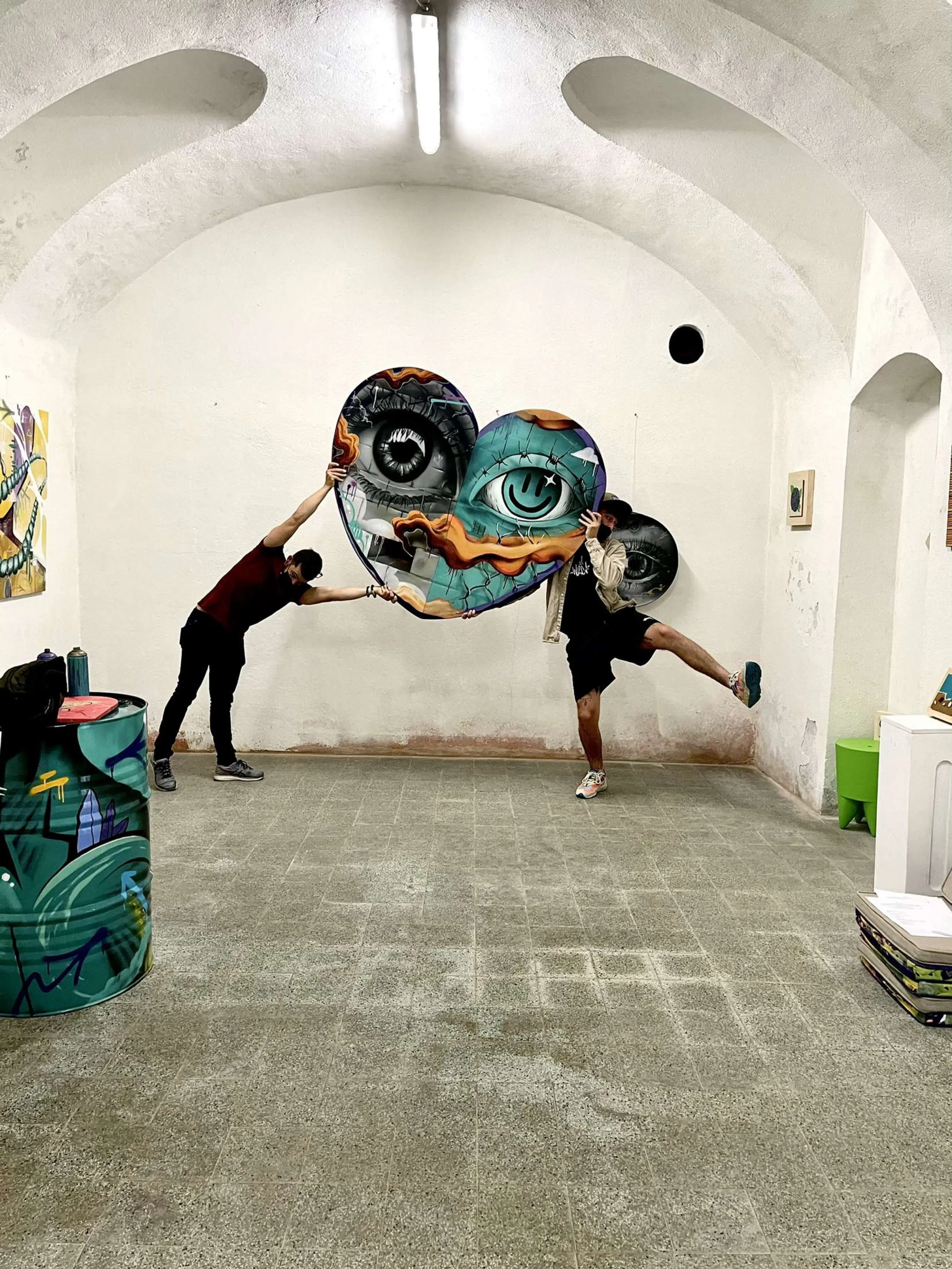Exposition en duo avec Karma Theora, galerie Noir & Blanc, 2021 : deux personnes tenant à bout de bras la toile en forme de cœur sous les voûtes de la galerie