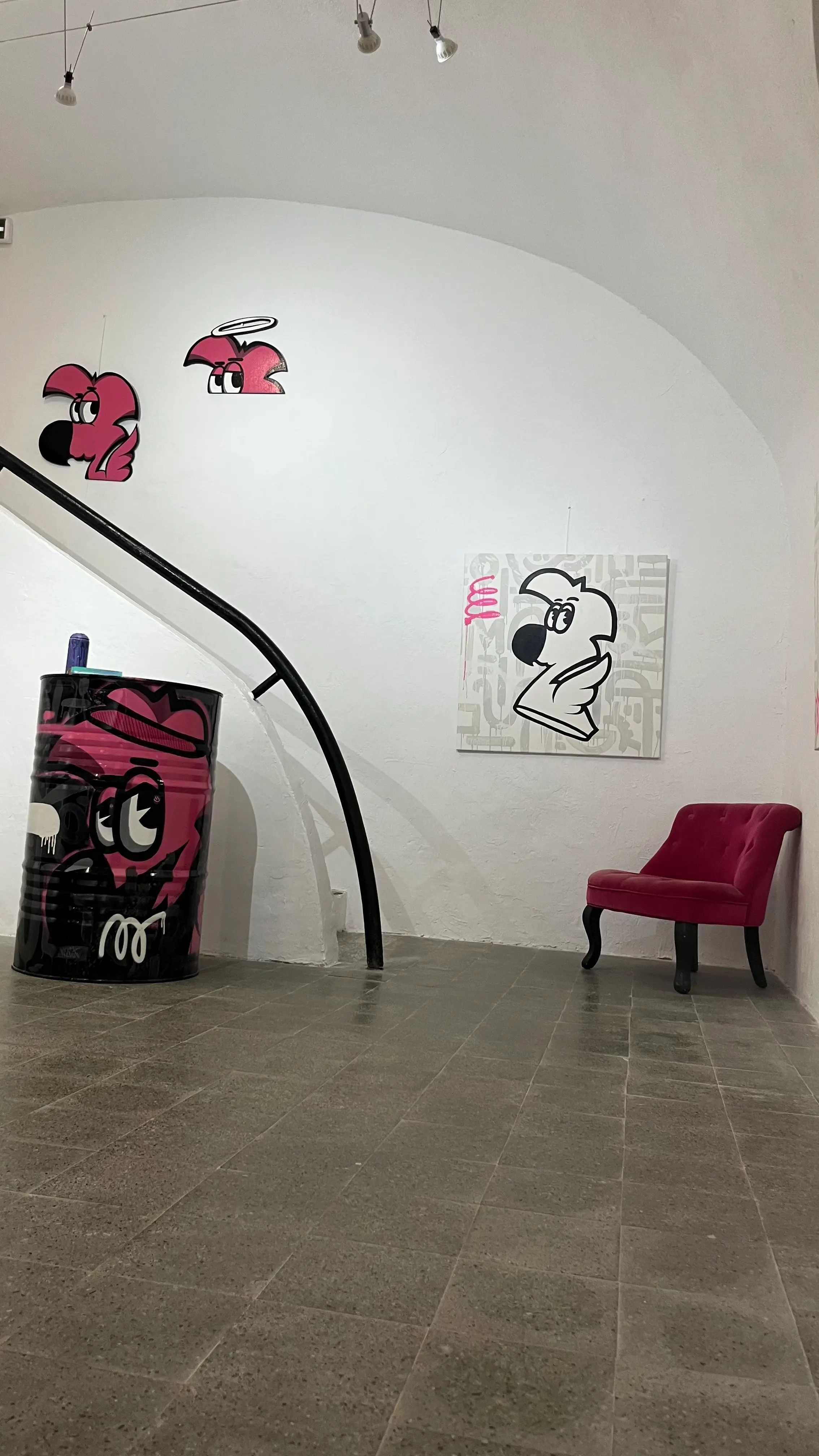 Exposition à la galerie Noir & Blanc, 2022 : salle voûtée, bidon peint en rose, découpes de Roger le Flamant Rose au mur et fauteuil rose