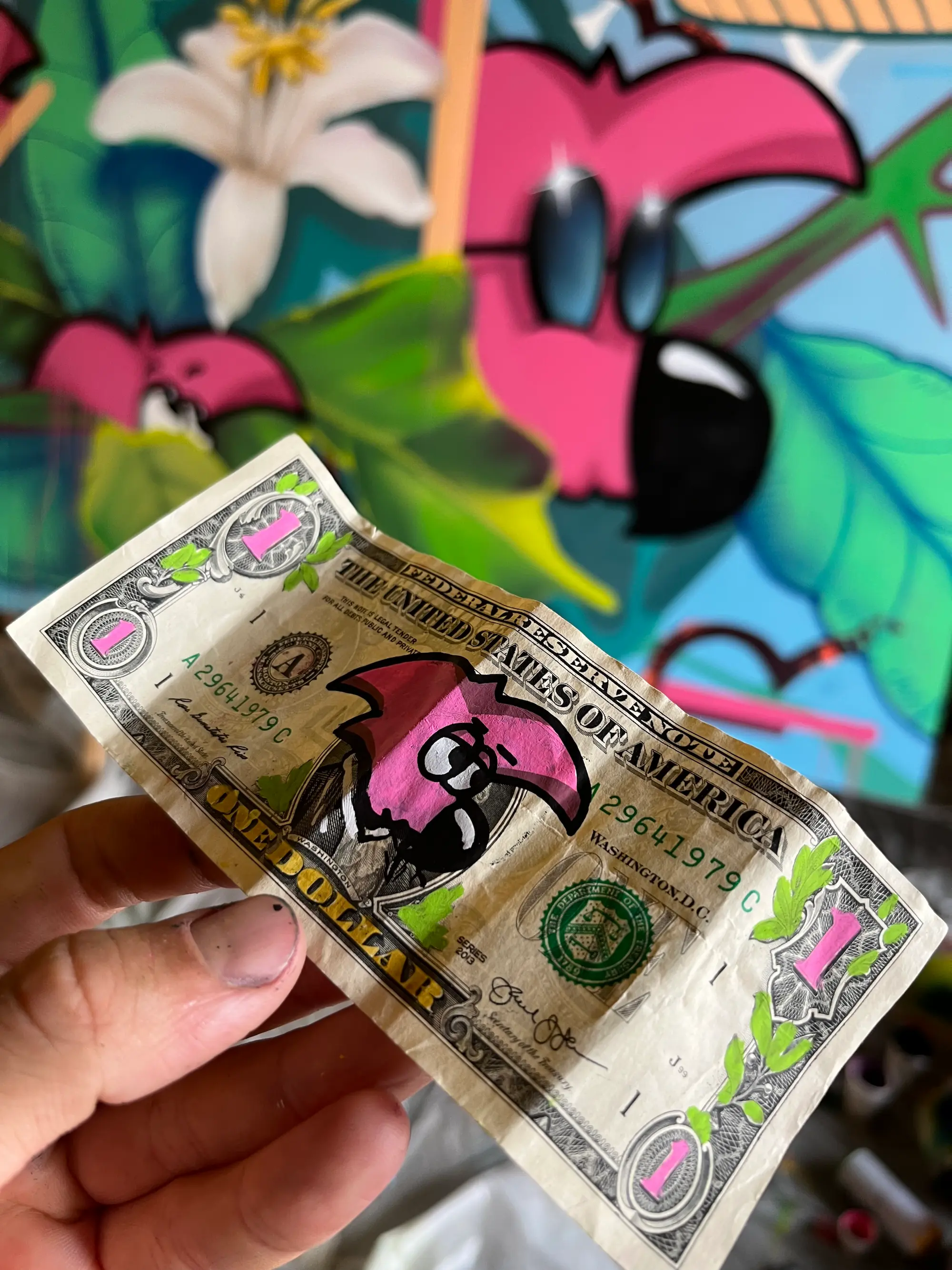 Live painting au festival Calviart, 2022 : billet d'un dollar customisé d'un Roger le Flamant Rose rose, tenu devant une fresque