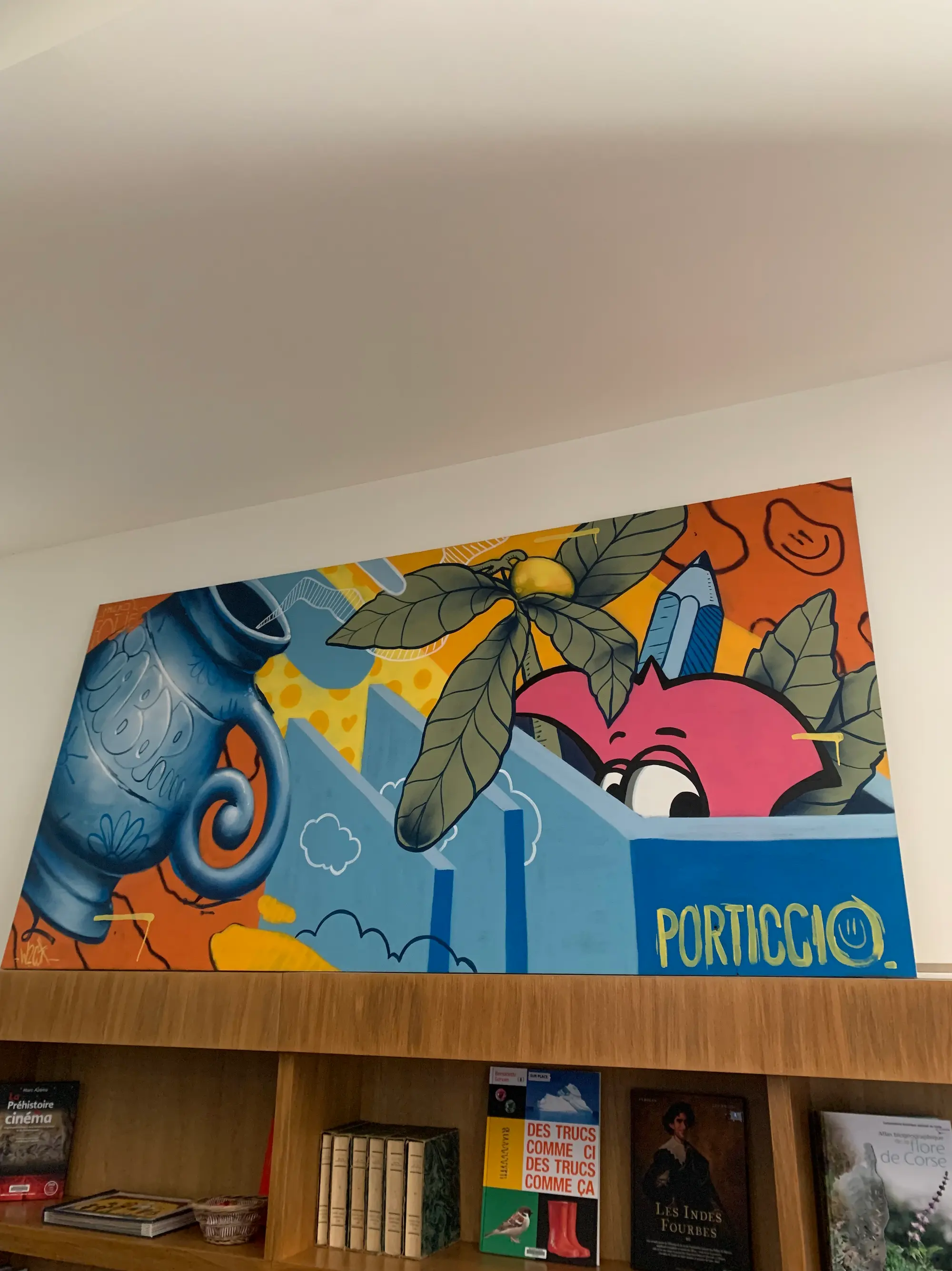Live painting à la médiathèque de Porticcio : toile accrochée au-dessus d'une bibliothèque, amphore bleue, Roger le Flamant Rose et le mot Porticcio