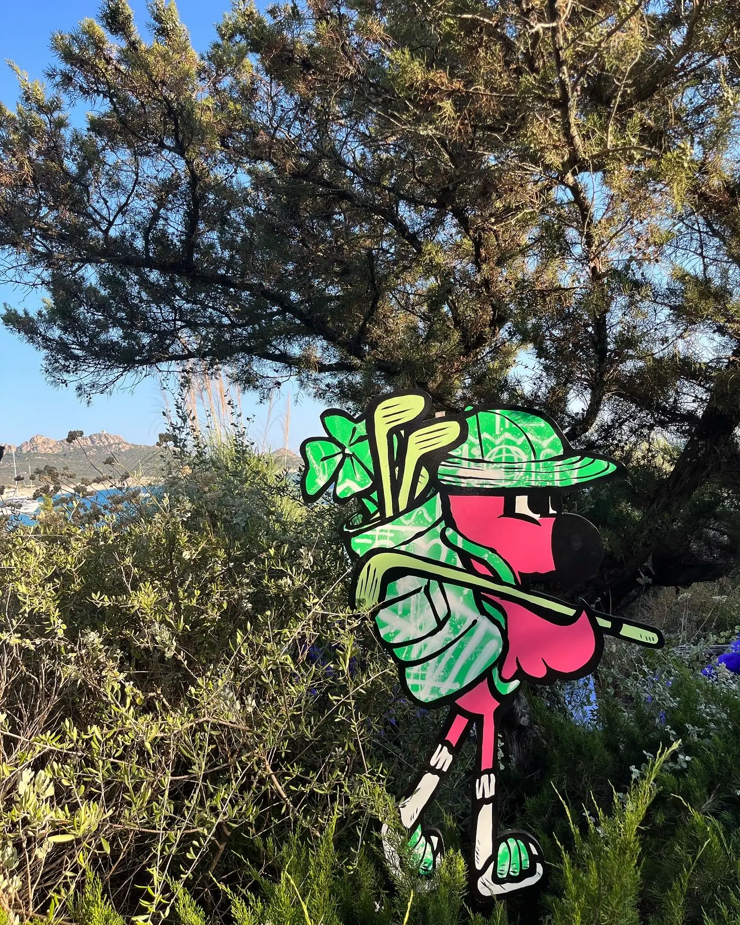 Exposition au Domaine de Murtoli, 2023 : découpe de Roger le Flamant Rose en golfeur, sac de clubs sur l'épaule, dans le maquis