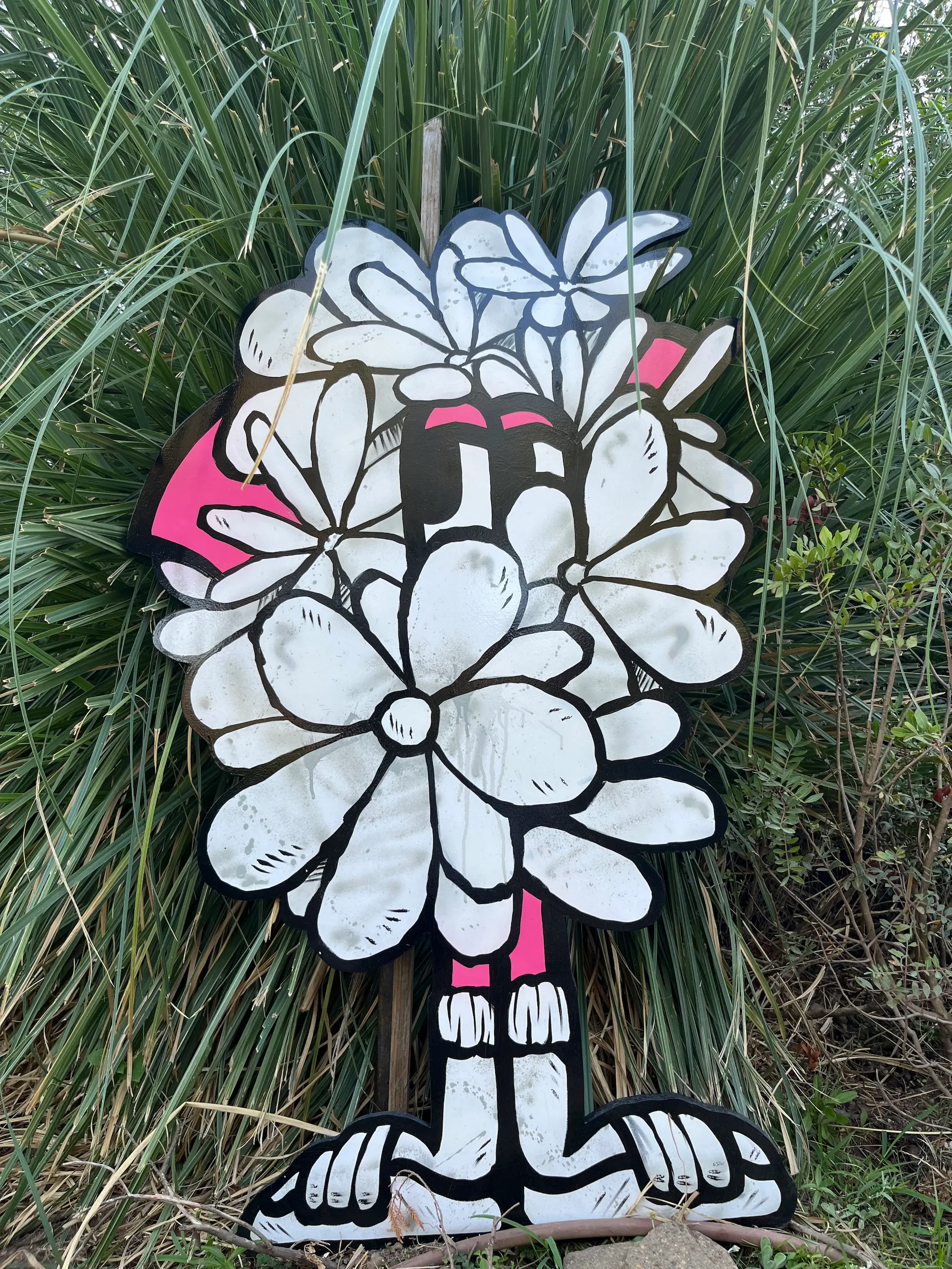 Exposition au Domaine de Murtoli, 2023 : découpe d'un Roger le Flamant Rose caché derrière un bouquet de fleurs blanches, devant des herbes hautes