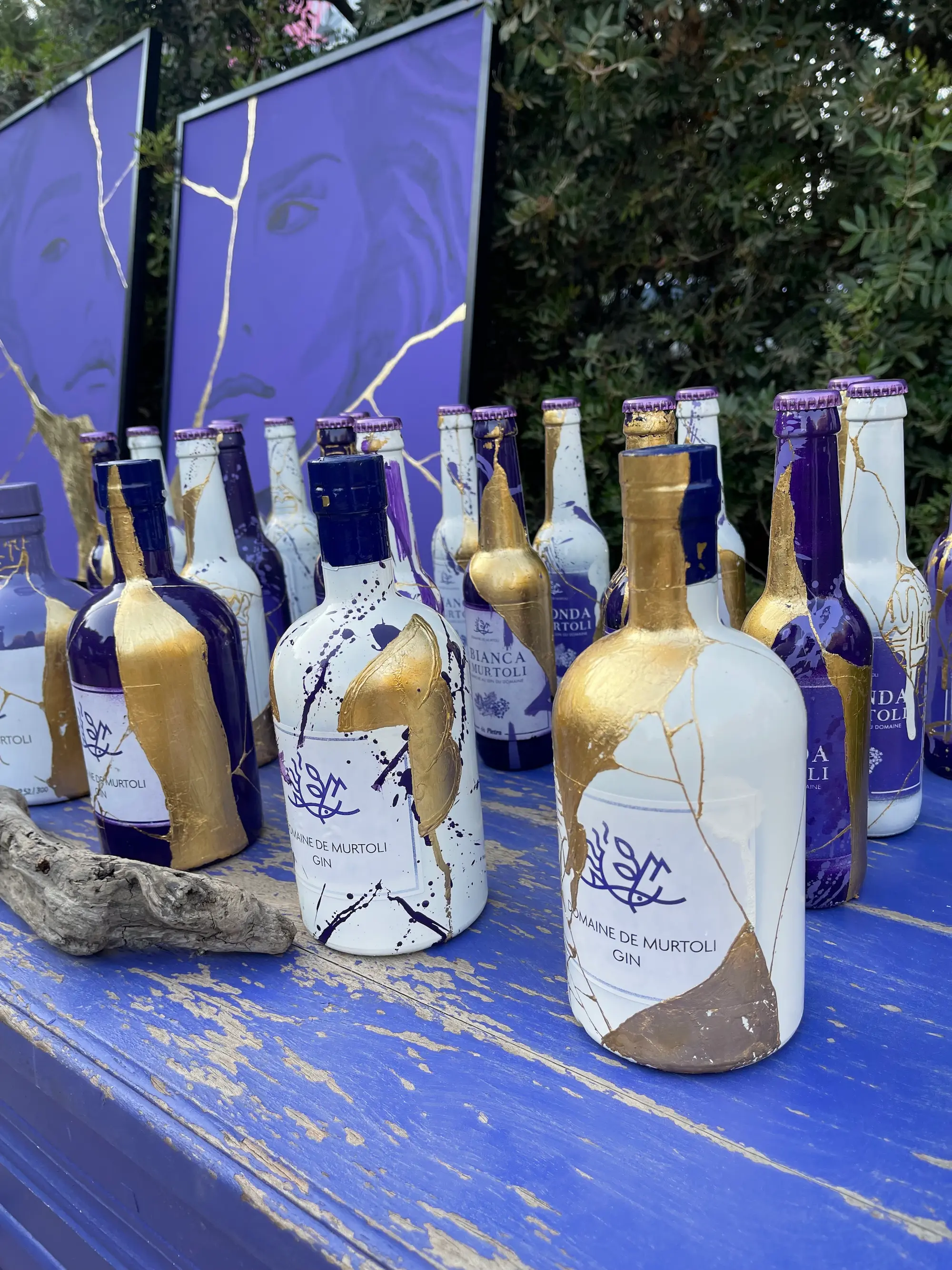Exposition au Domaine de Murtoli, 2023 : bouteilles de gin du domaine décorées de feuille d'or, alignées sur une table bleue