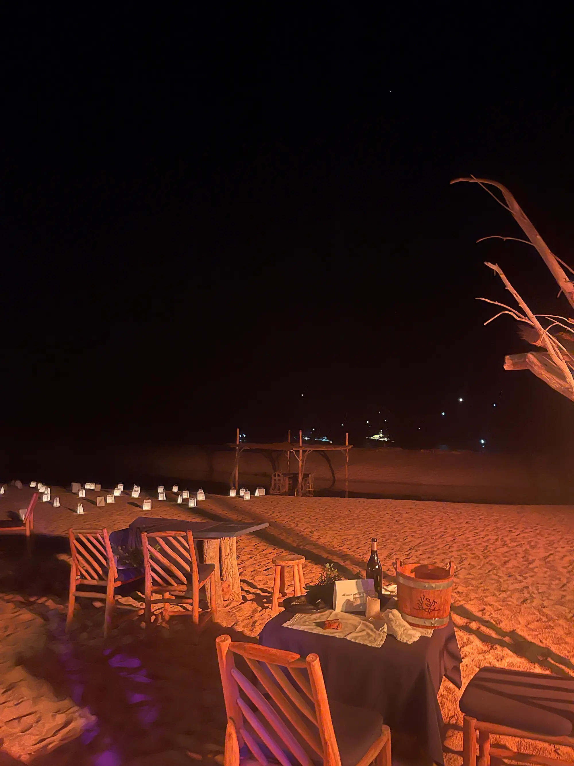 Exposition au Domaine de Murtoli, 2023 : tables dressées sur la plage de nuit, lanternes alignées sur le sable