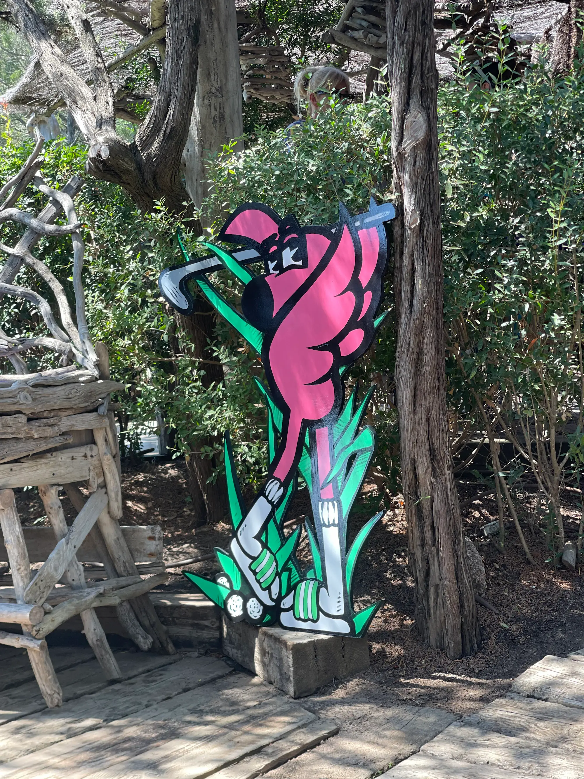 Exposition au Domaine de Murtoli, 2023 : découpe de Roger le Flamant Rose jouant au golf, posée sur un socle en bois dans le jardin