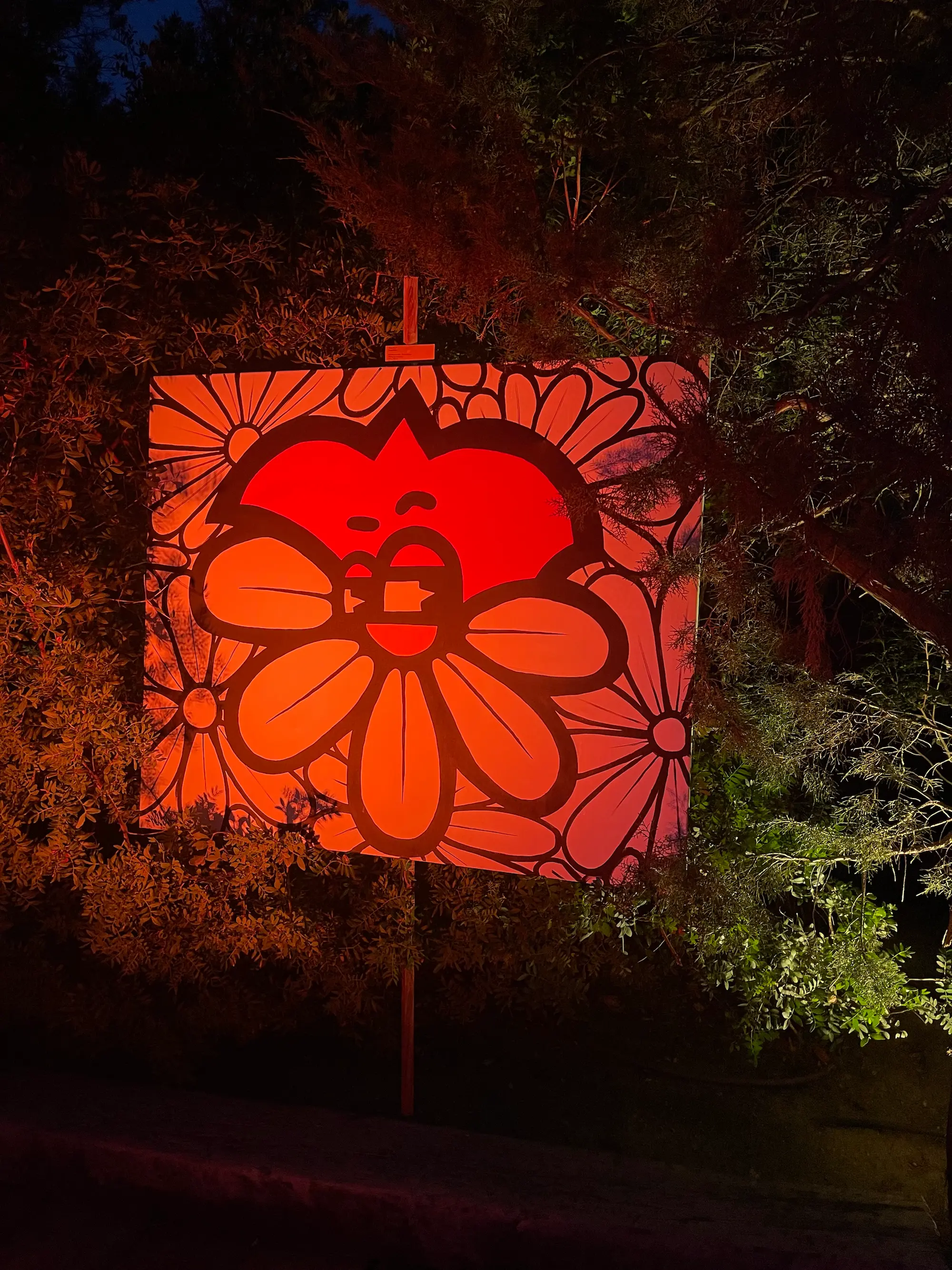 Exposition au Domaine de Murtoli, 2023 : toile du cœur souriant aux fleurs éclairée en rouge dans les arbres, de nuit