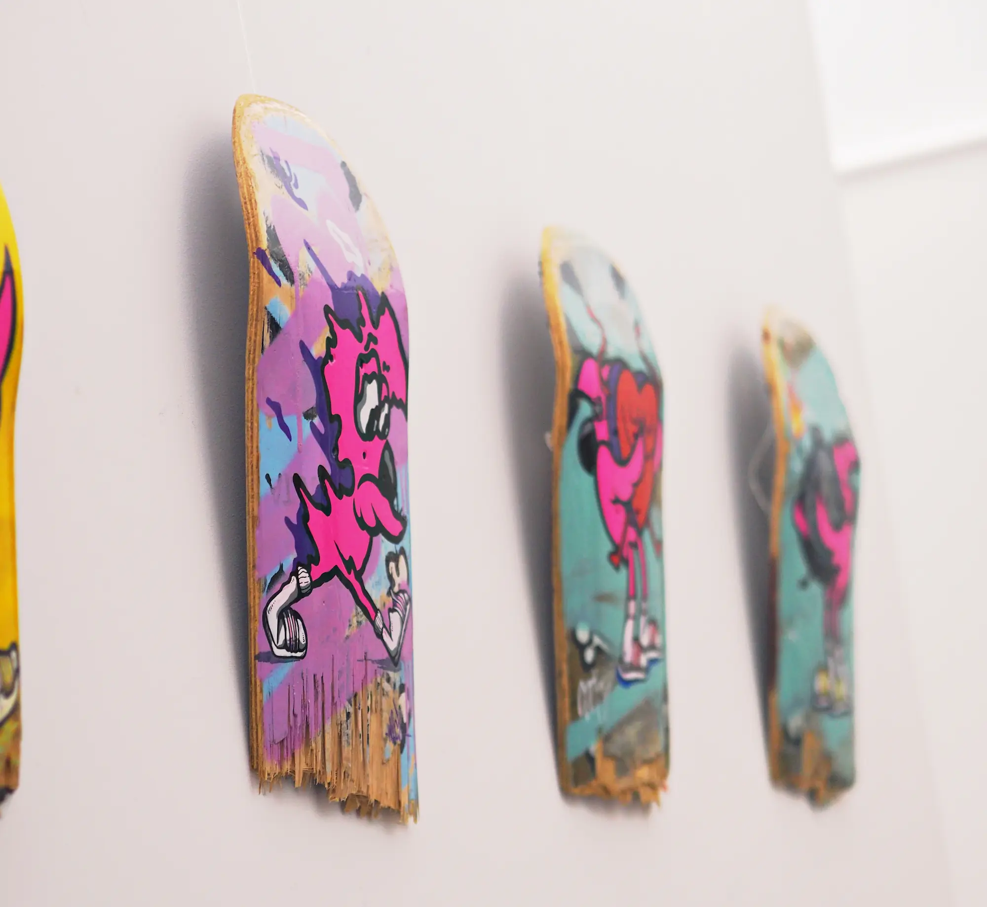 « Vision », exposition en duo, 2023 : plateaux de skate peints de Roger le Flamant Rose accrochés en ligne sur un mur blanc