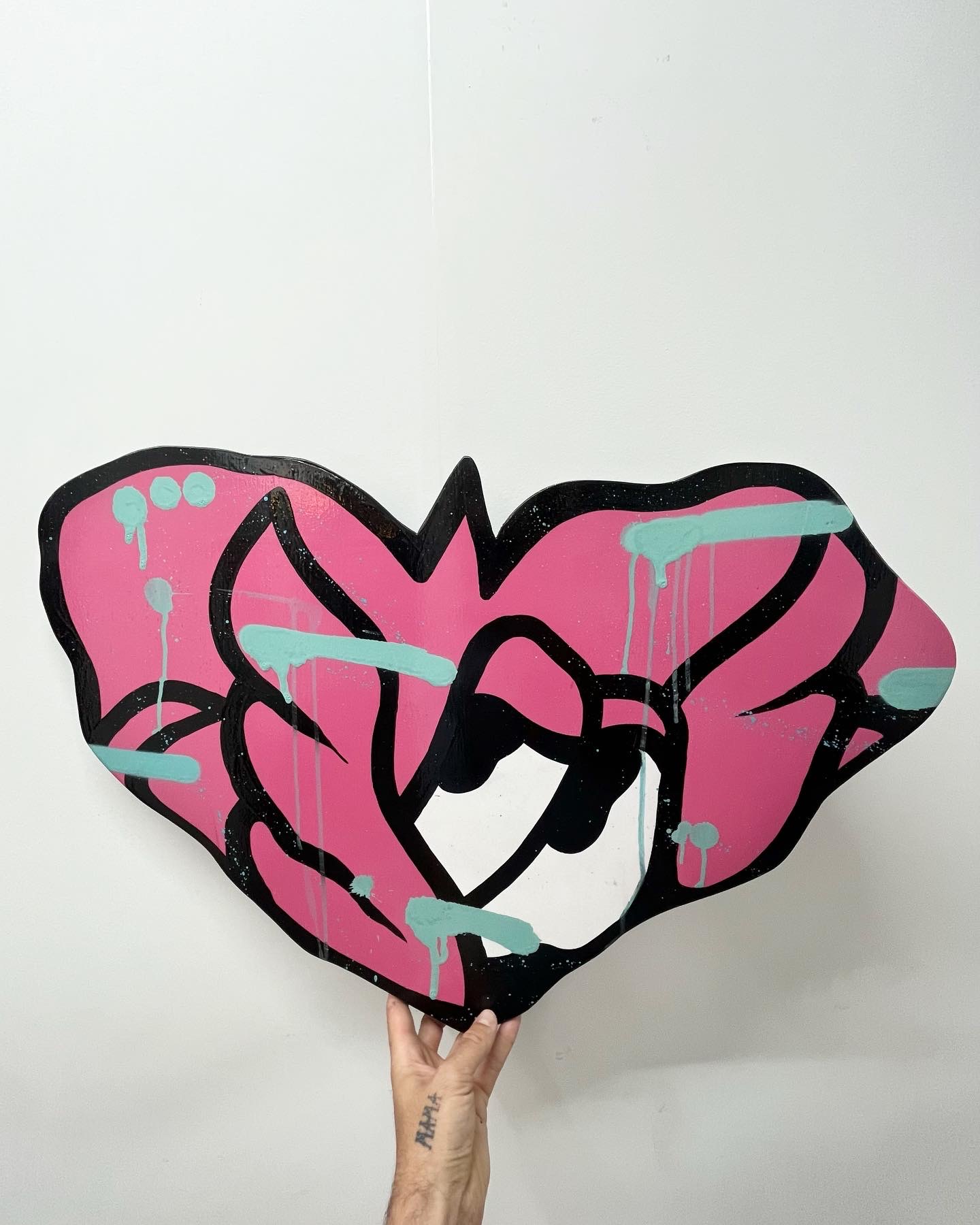« Vision », exposition en duo, 2023 : découpe en forme de cœur rose aux coulures turquoise, tenue à bout de bras devant un mur blanc