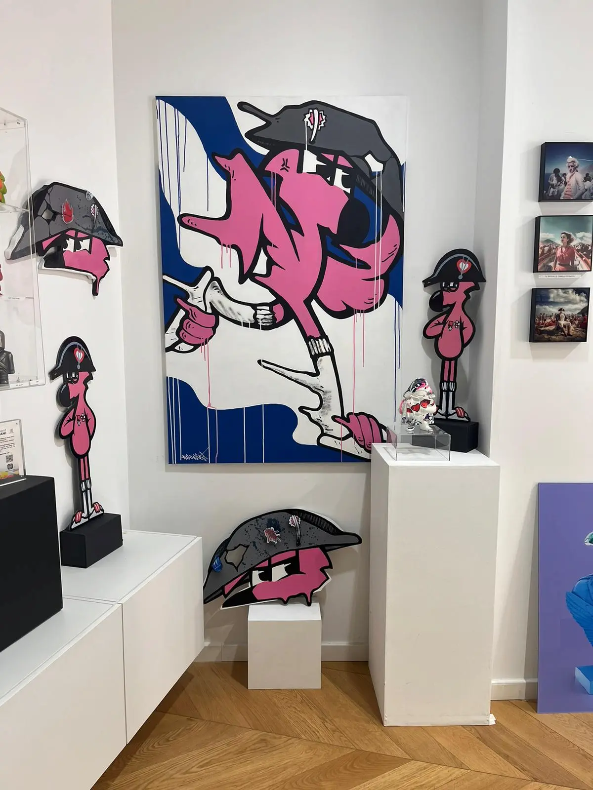 Exposition Contami, 2024 : accrochage en galerie : toile de Roger le Flamant Rose en Napoléon, découpes et sculptures sur socles blancs