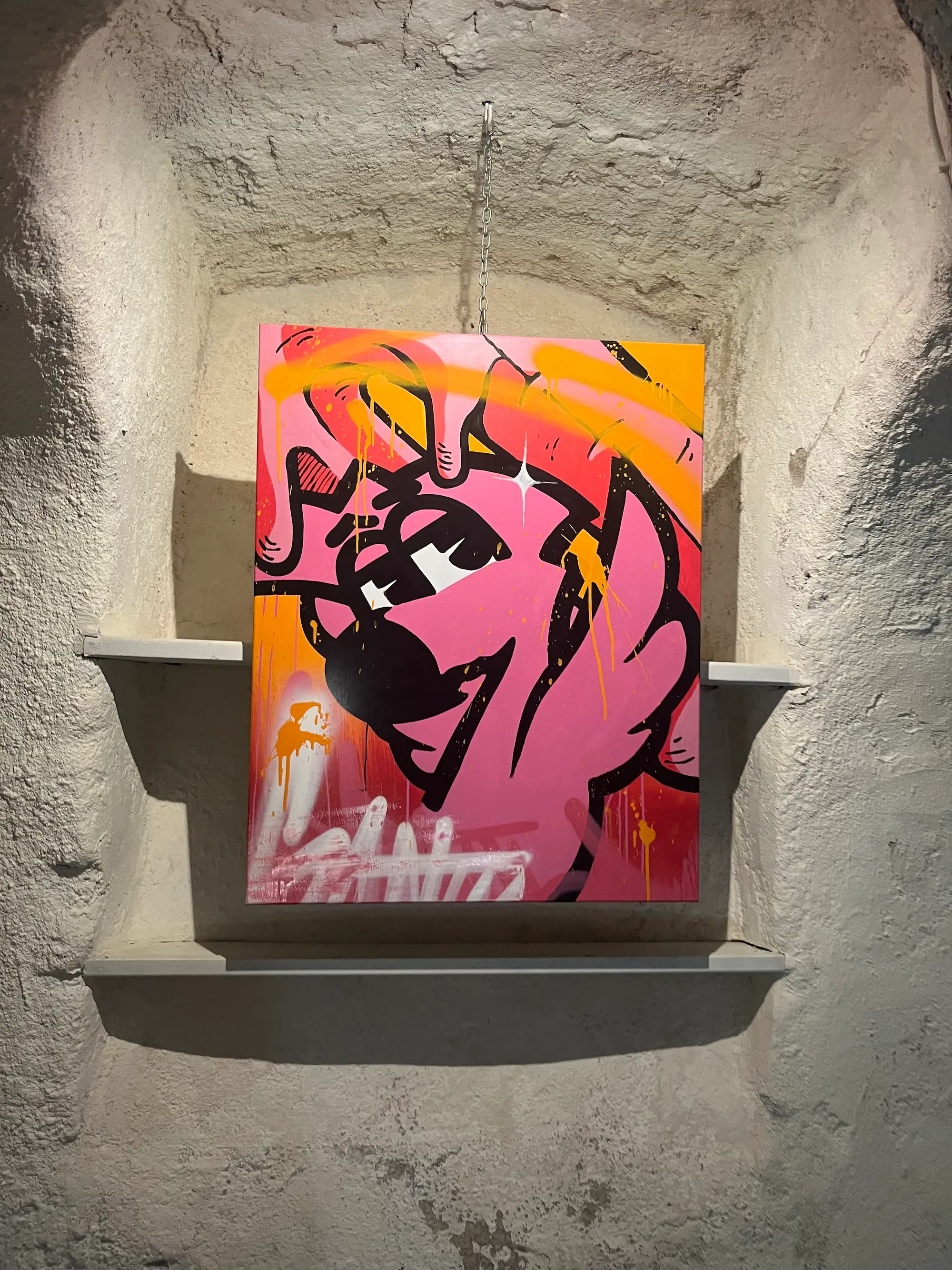 Exposition collective à la Capu Galerie, 2024 : toile rose et orange de Roger le Flamant Rose accrochée dans une niche en pierre