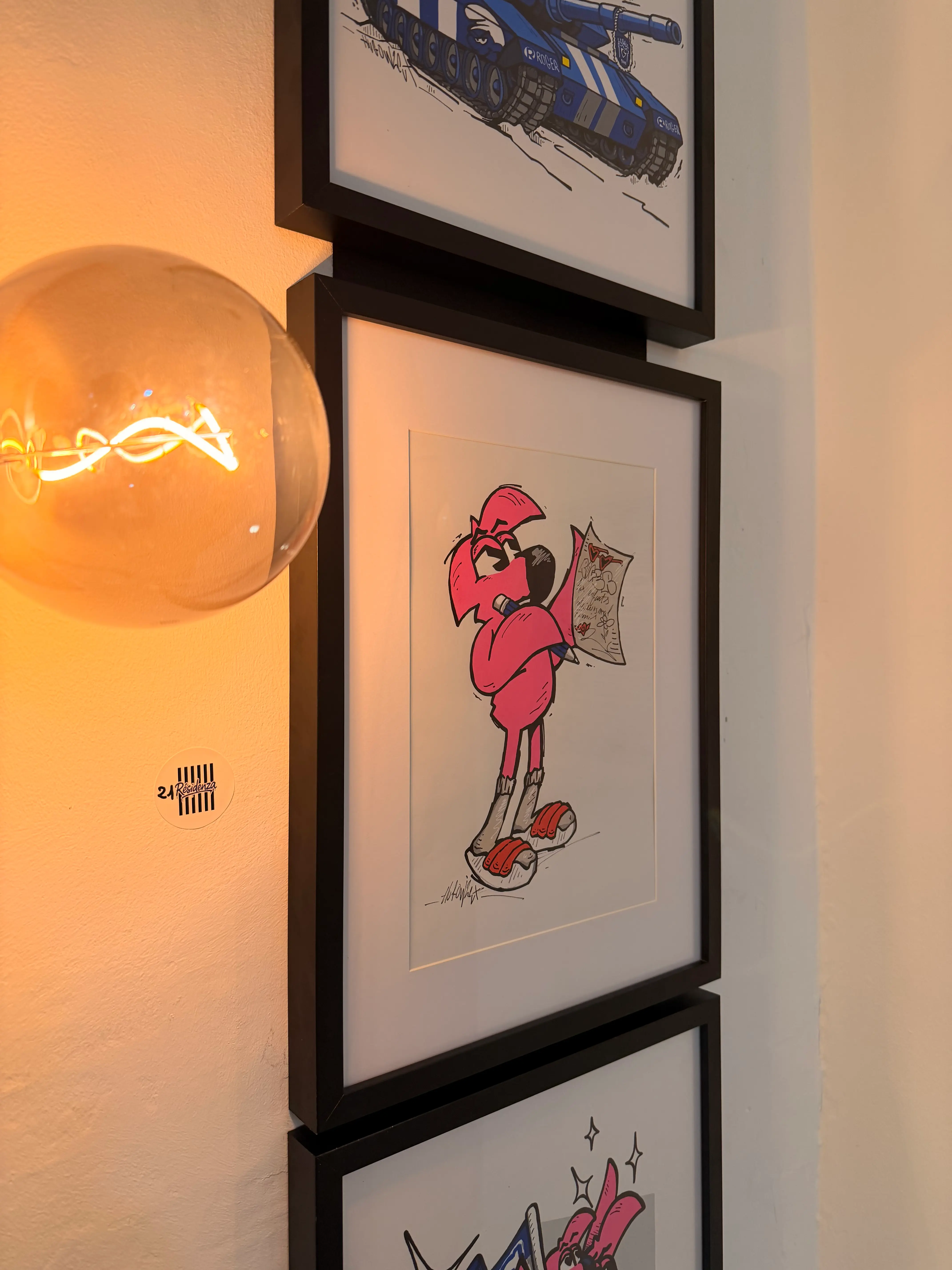 Street Therapy, exposition de Hugo W2CJ, 2026 : dessins encadrés accrochés en colonne, Roger le Flamant Rose tenant une feuille, près d'une lampe