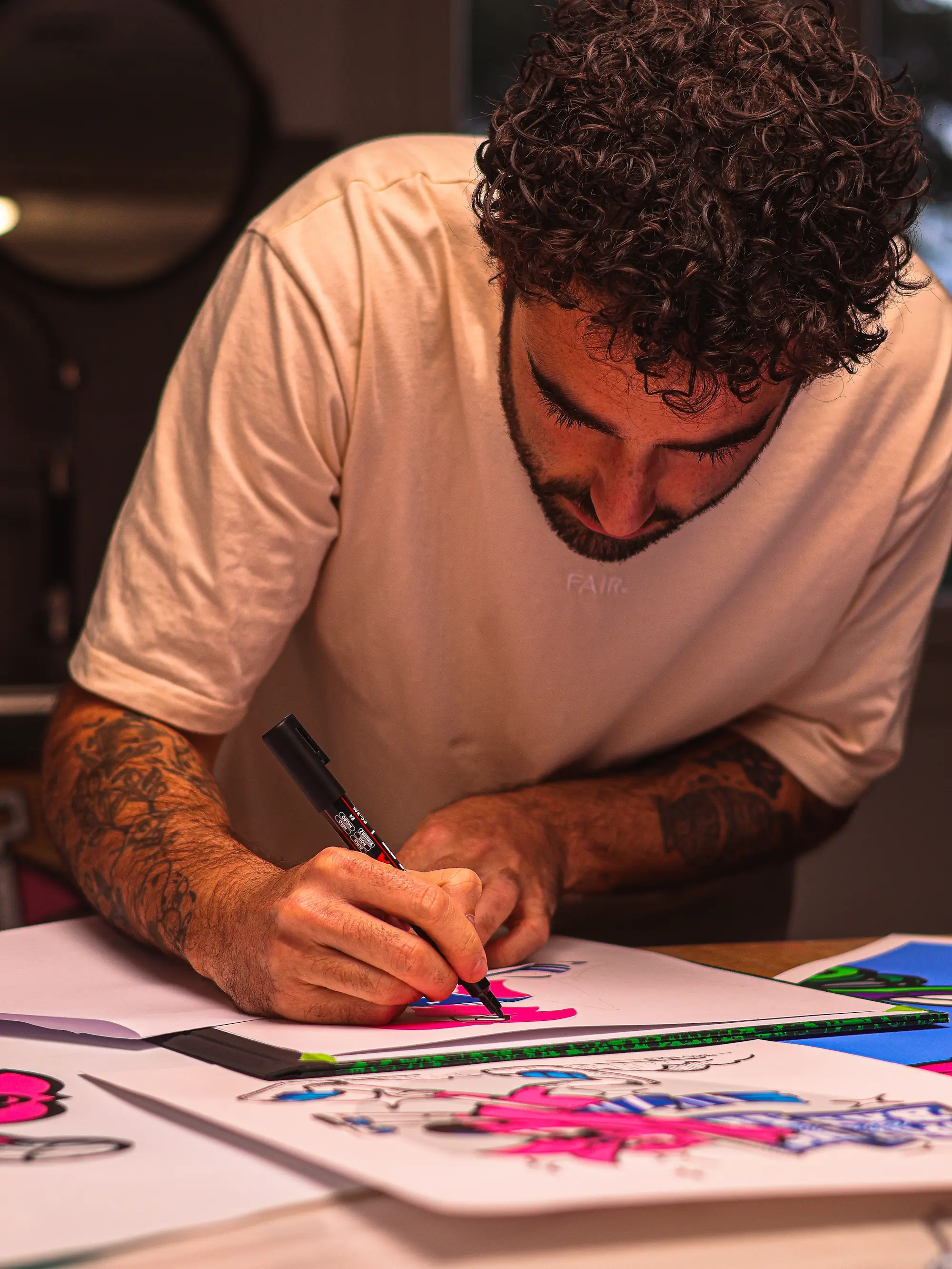 Collaboration Hugo W2CJ x Sporting Club de Bastia : l'artiste dessinant au marqueur sur une table couverte de dessins