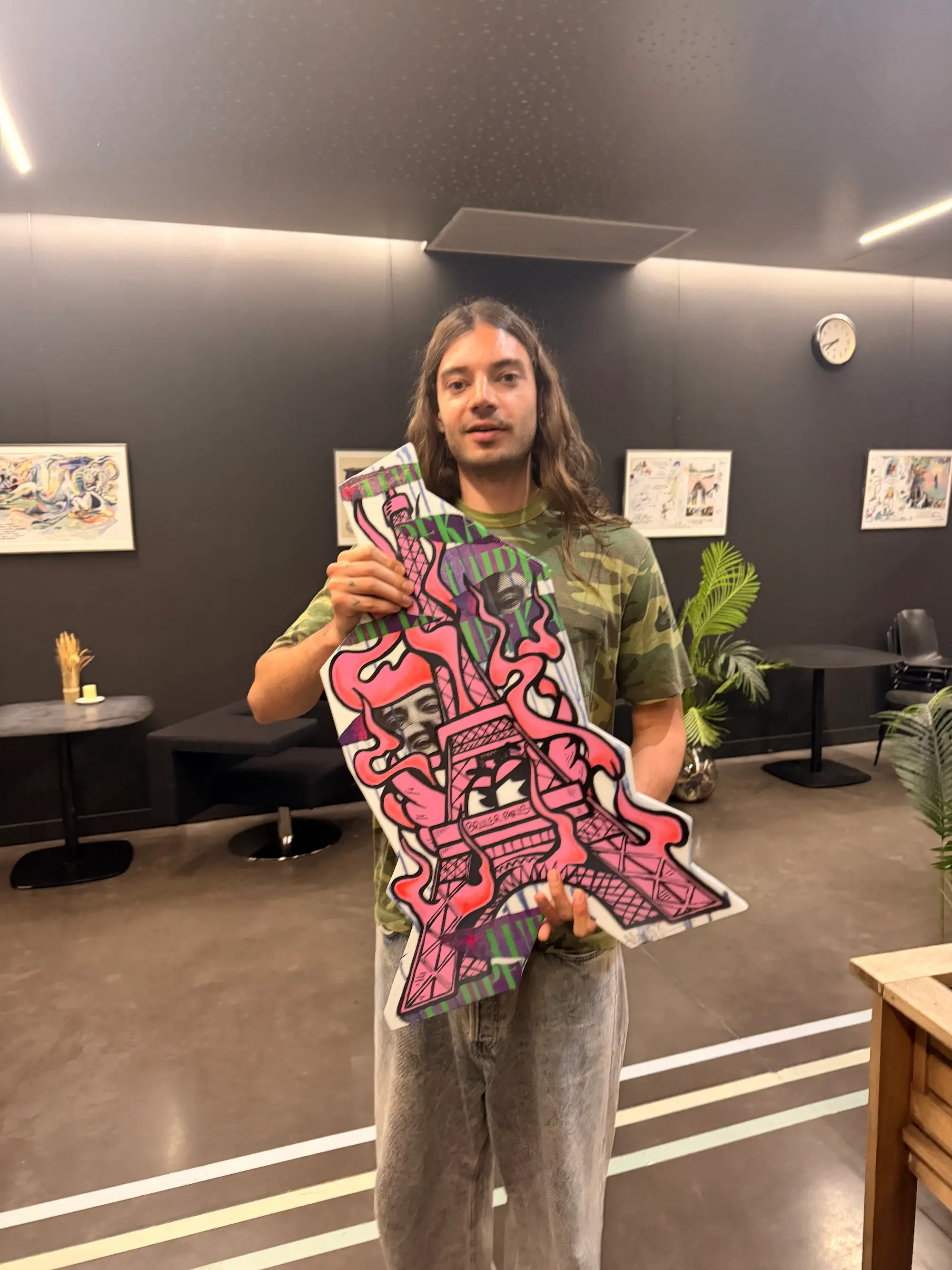 Lujipeka, artiste du festival East Side 2026, tenant une sculpture murale peinte par Hugo W2CJ : Roger le Flamant Rose en tour Eiffel, clin d'œil à son album Brûler Paris