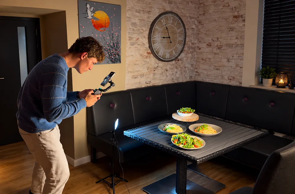 Tom Agge filmt Gerichte auf einem gedeckten Tisch mit dem Smartphone