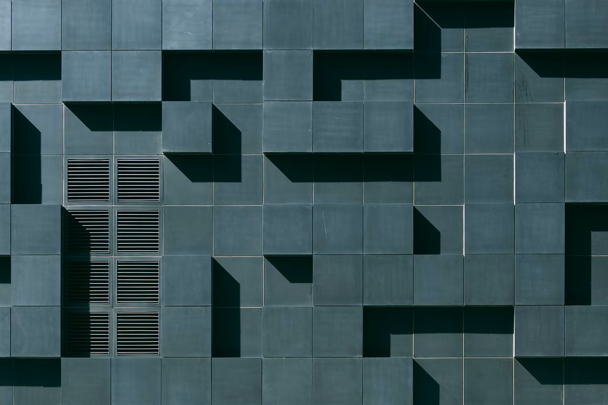 Pattern of dark square wall panels with some protruding to form shadows and a side vent.