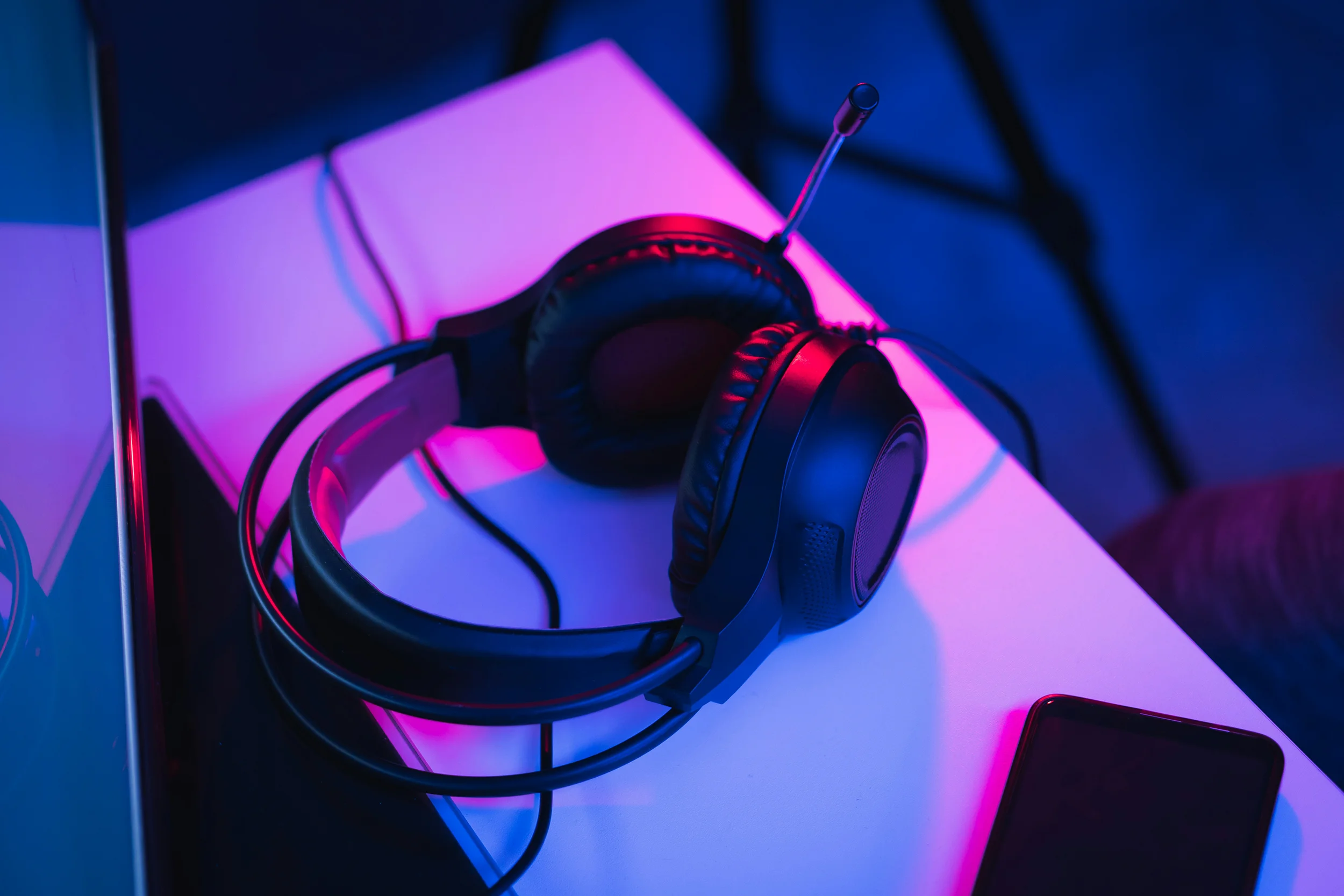Headphones on a desk in a vibrant blue and pink-lit workspace