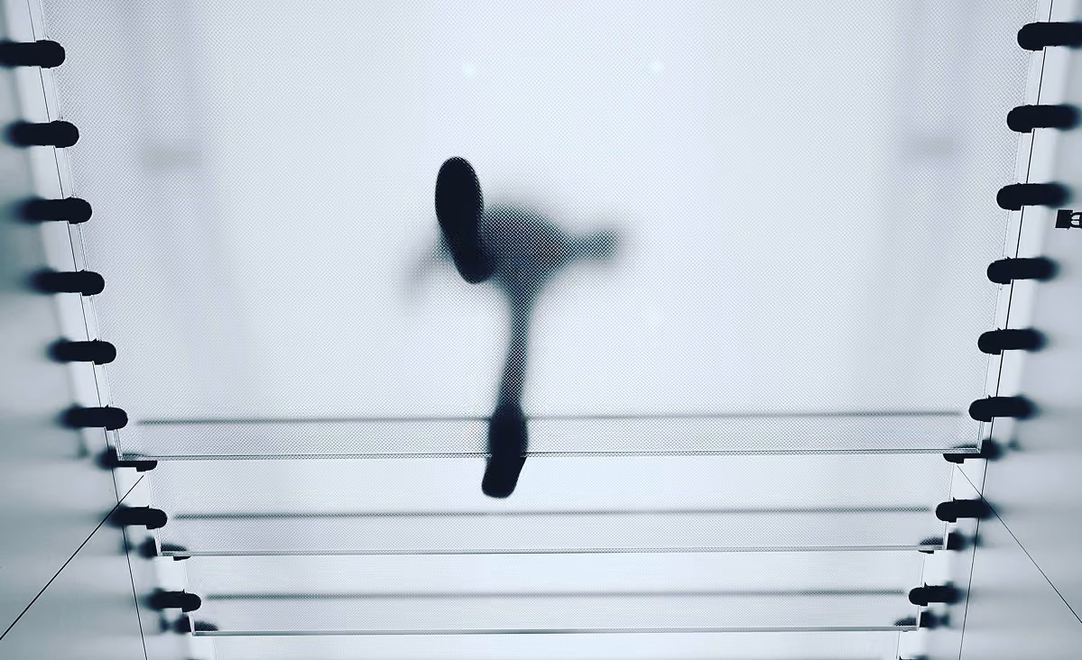 Silhouette of a person walking on a suspended glass bridge viewed from below.