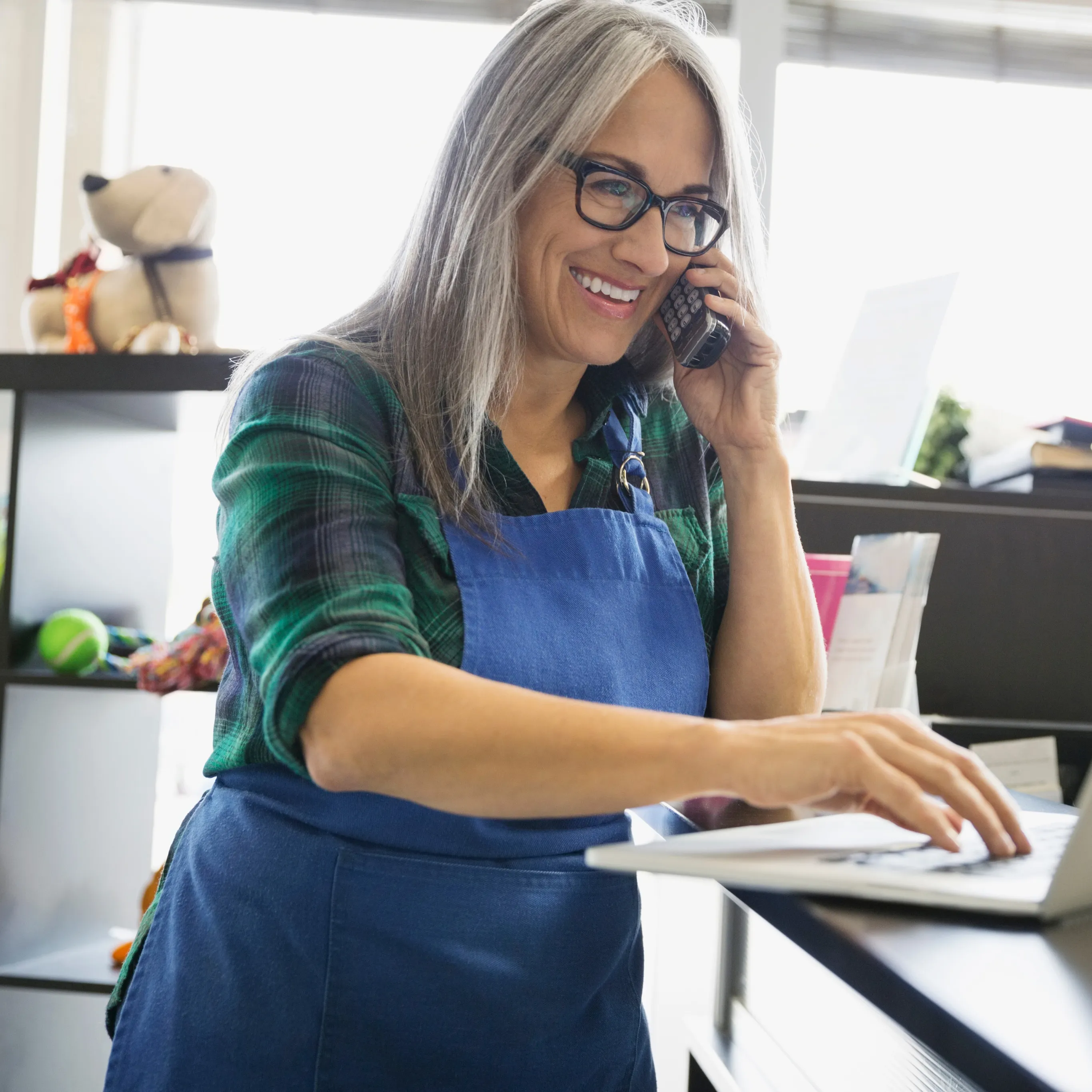 a woman at work, talking on the phone and typing on the laptop
