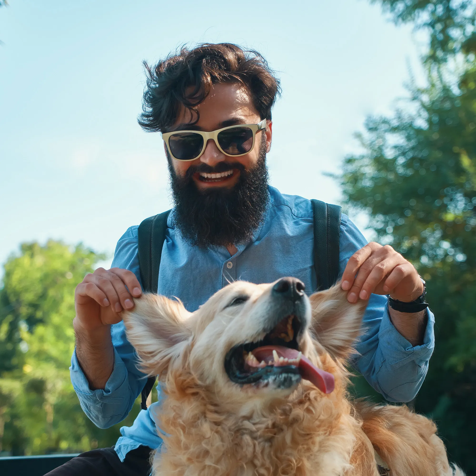 a man in the outdoors, playing with the ears of his dog