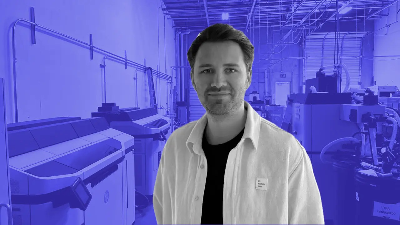 Something Added team member in a white coat on the floor of the Barcelona 3D printing factory, rows of printers behind.