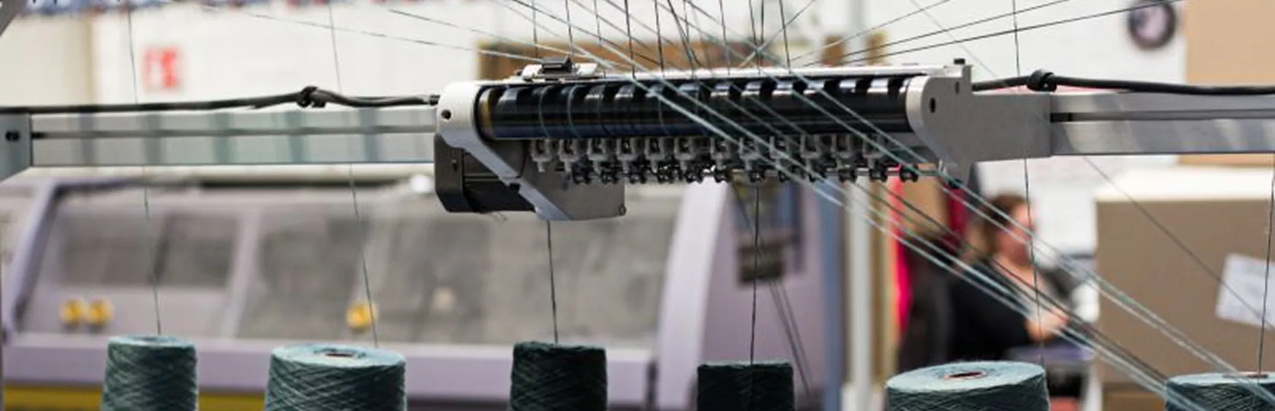 Close up of a textile weaving machine with yarn threads and spools in a factory.