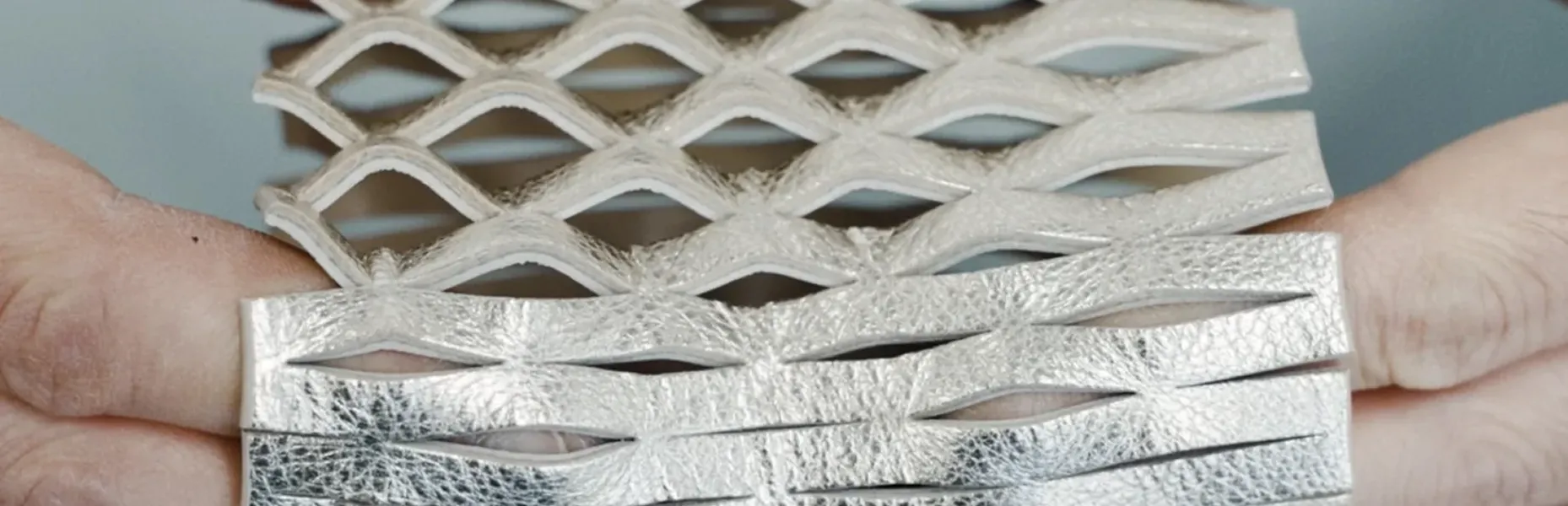Hands stretching a metallic diamond mesh material into an expanded pattern.