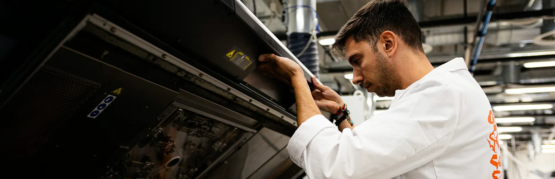 A man in a white lab coat inspecting industrial machinery in a factory.