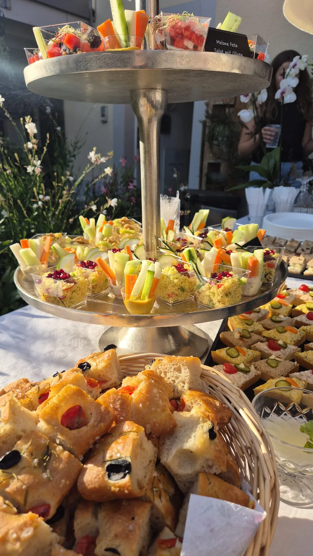 Apérohäppchen auf einer Etagere zwischen Blumendekorationen
