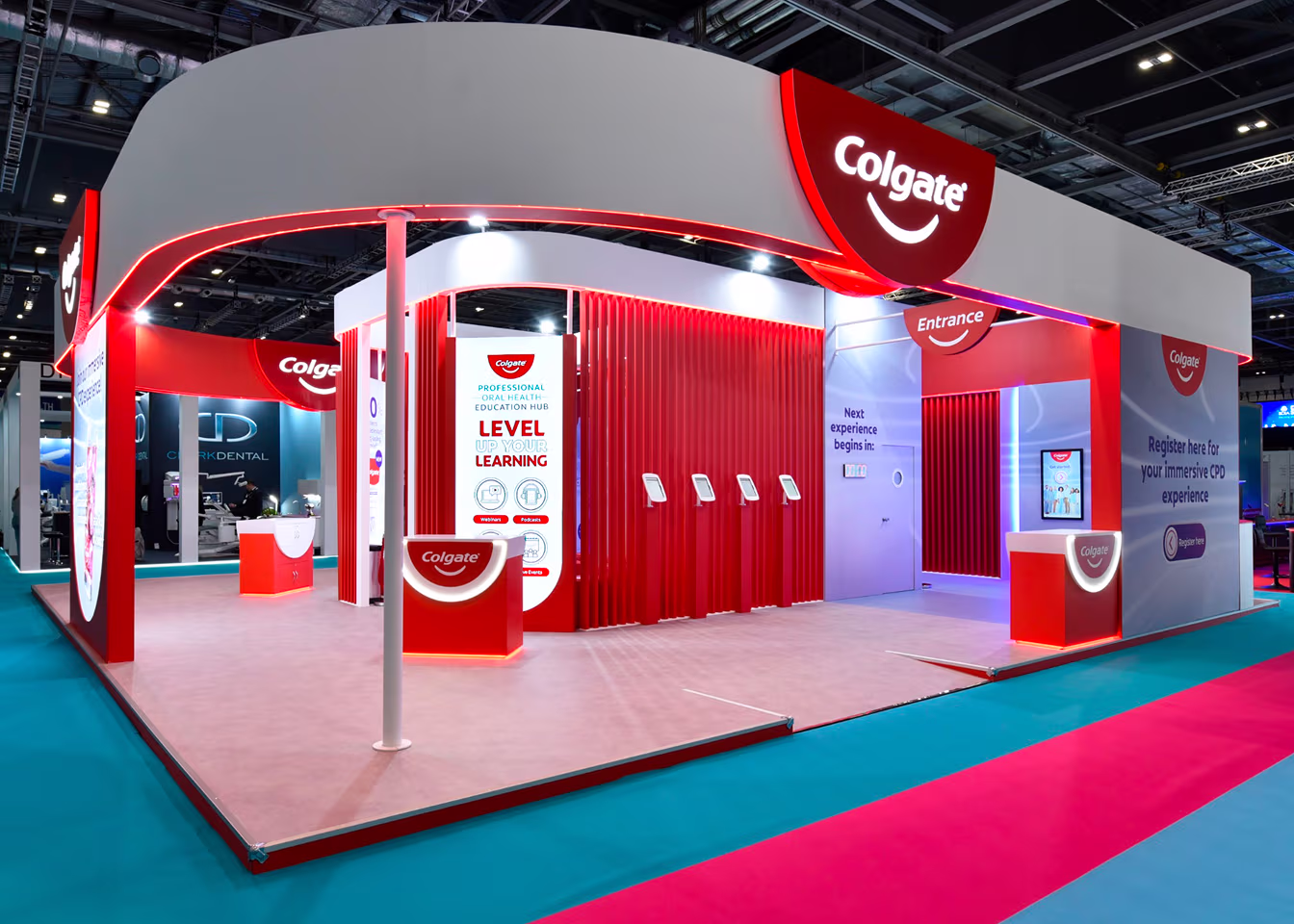 Colgate-branded exhibition booth with red and white design, digital displays, and tablet stands.