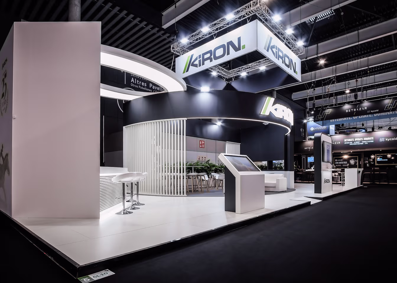 Modern exhibition booth with Kiron branding, white stools, and digital display at trade show.