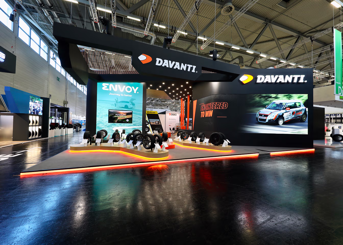Davanti tire display booth with tires and screens showing Envoy and race car images at an indoor trade show.