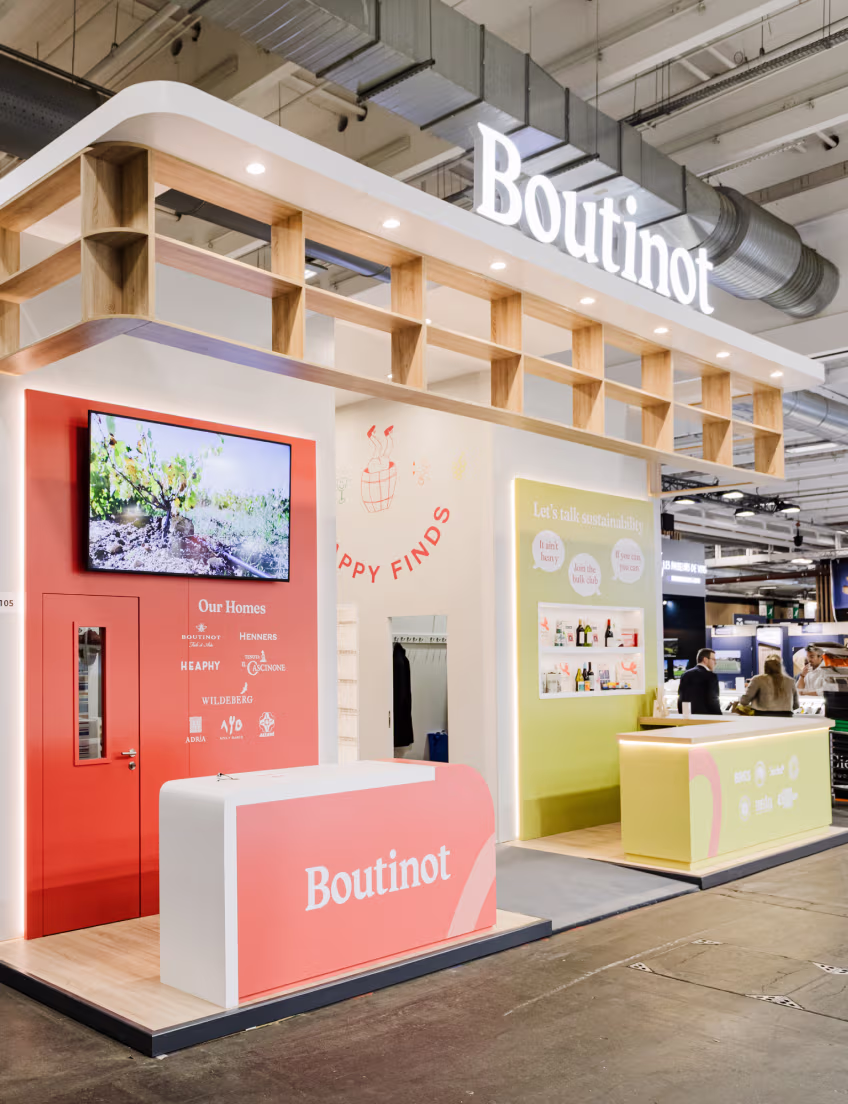 Modern exhibition booth for Boutinot wine with pink and yellow counters and a vine video on screen.