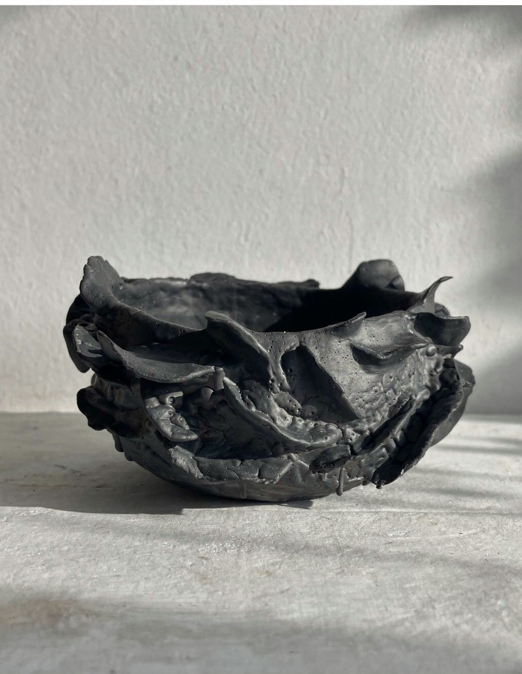 Low hand-built ceramic bowl in dark charcoal clay with a torn, jagged rim, by Consuelo Becerra