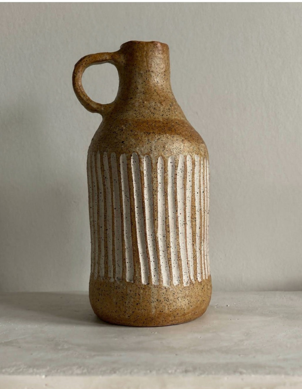 Hand-built ceramic bottle in ochre stoneware with carved white vertical lines and speckled glaze, by Consuelo Becerra